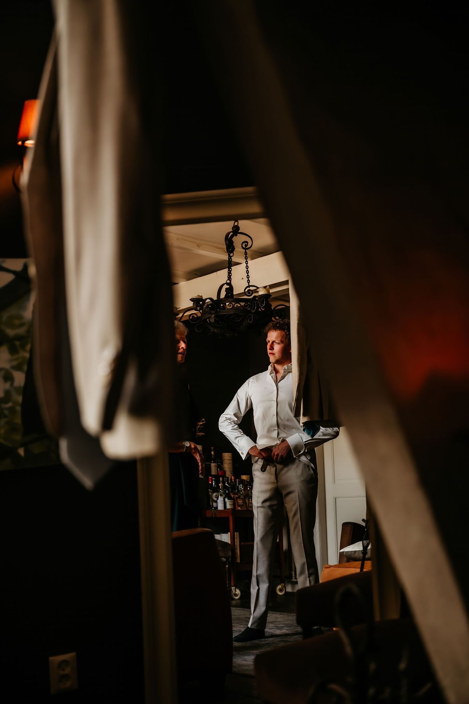 Wedding preparations captured through doorway frames with moody lighting.