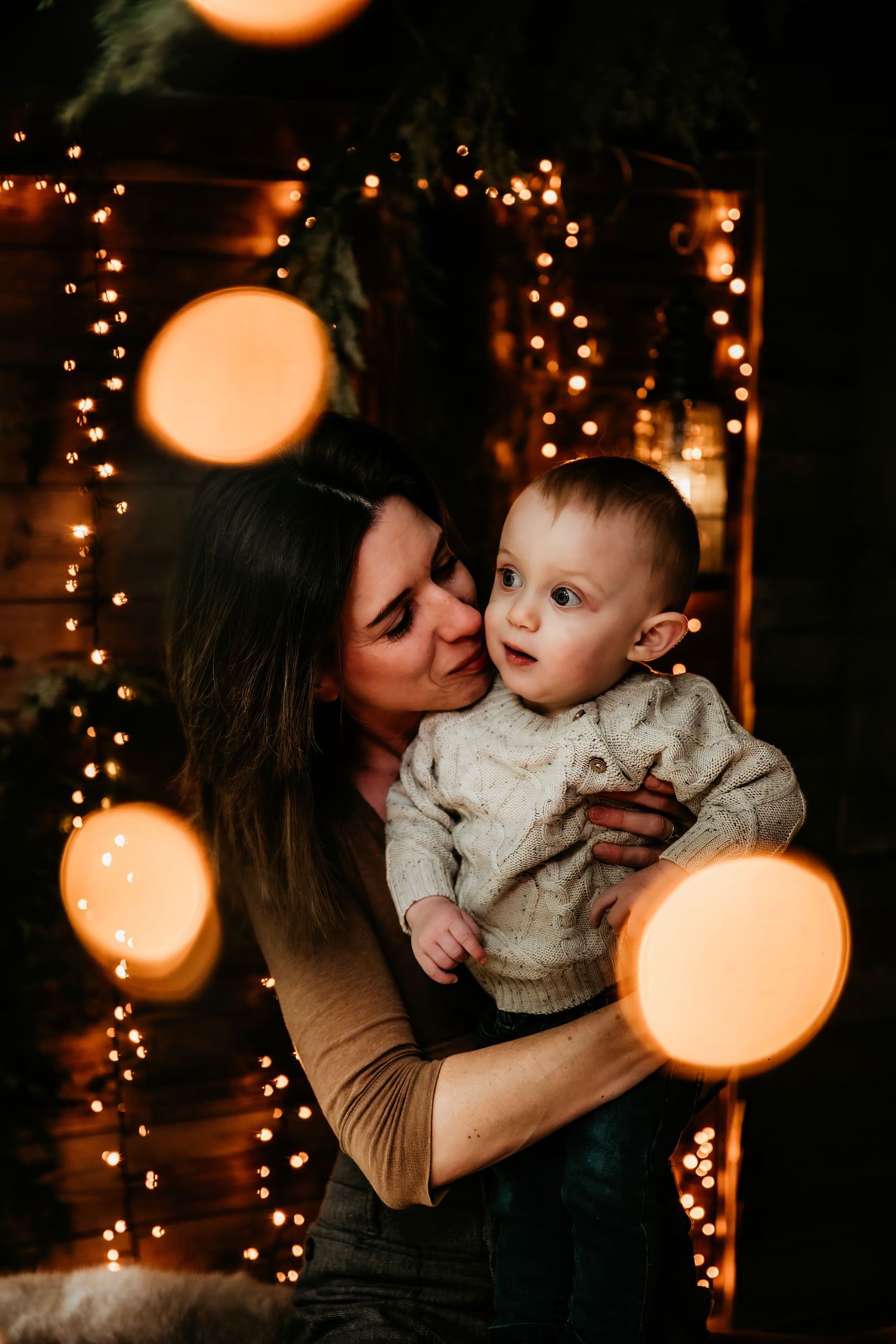 A tender moment shared between parent and child against a backdrop of glowing holiday lights and bokeh effects.