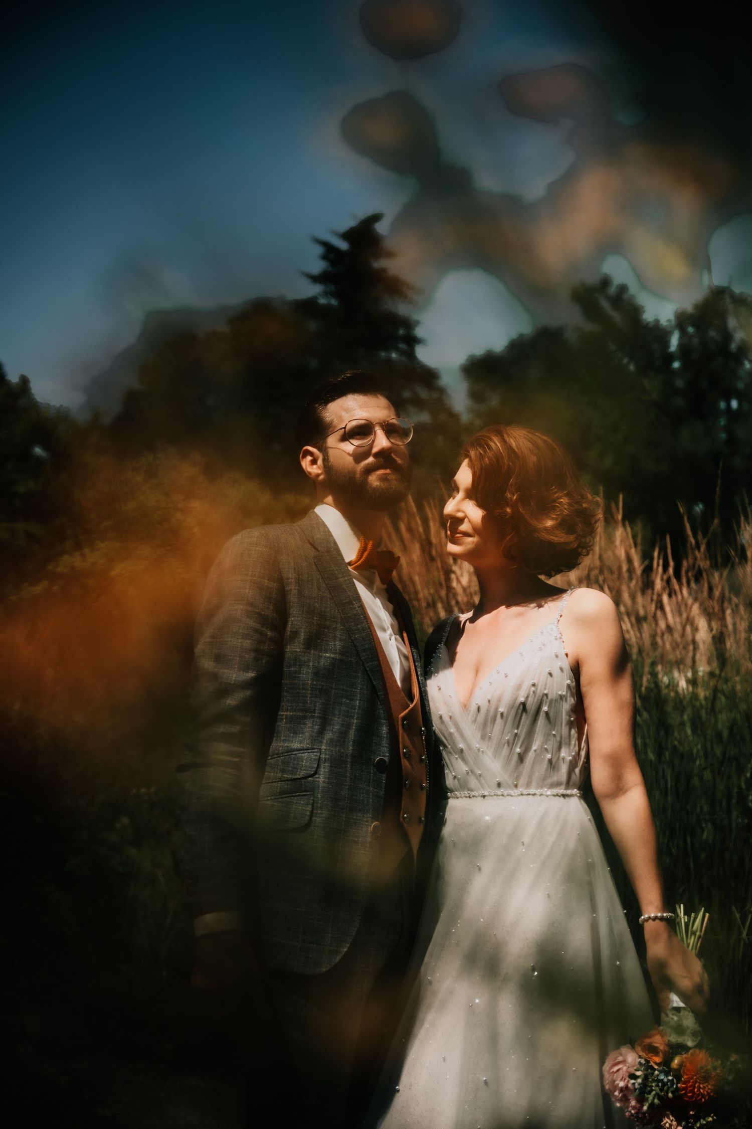 A romantic outdoor wedding photoshoot at sunset with moody lighting and tall grass in the background.