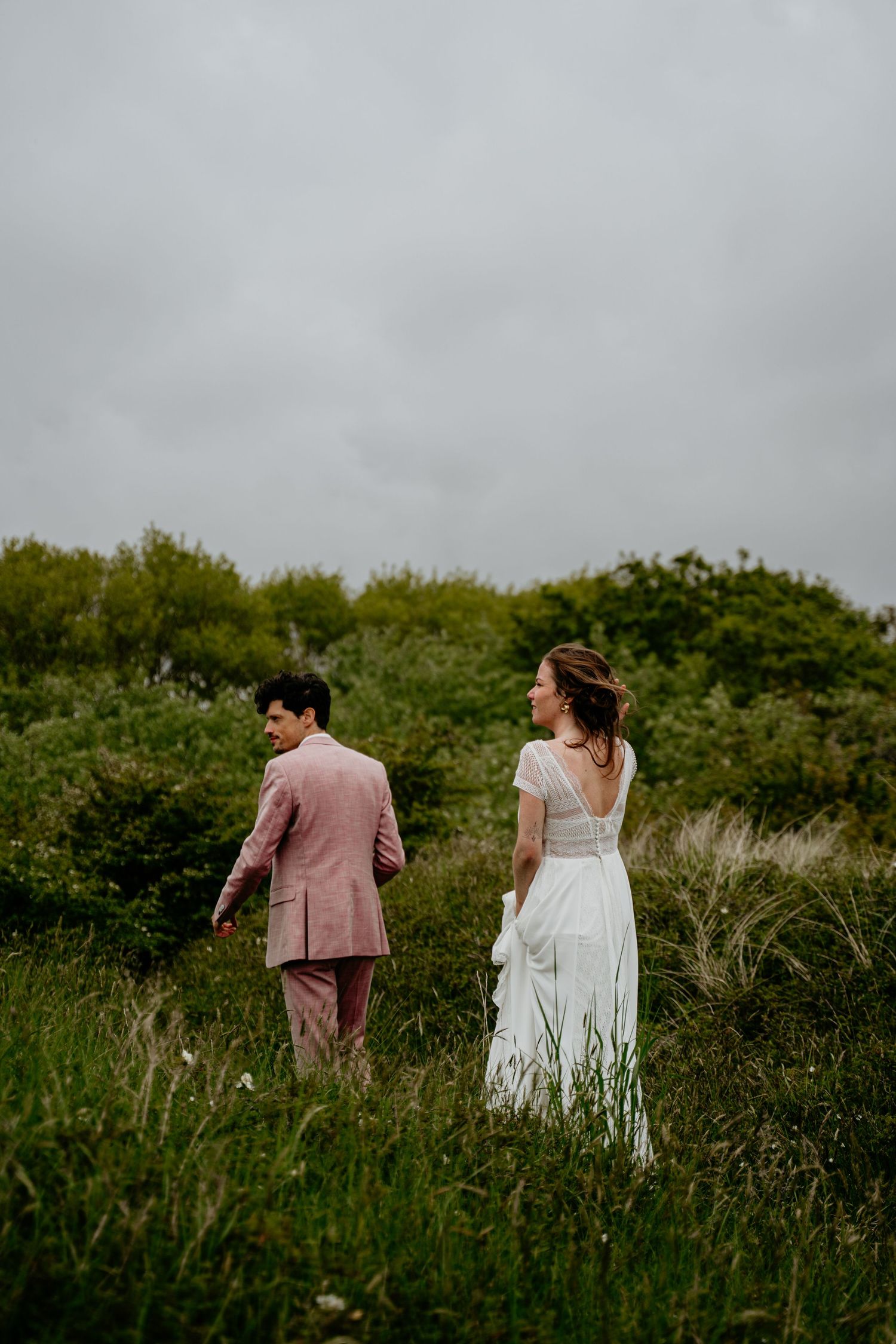 Couple walking through tall grass field on overcast day.