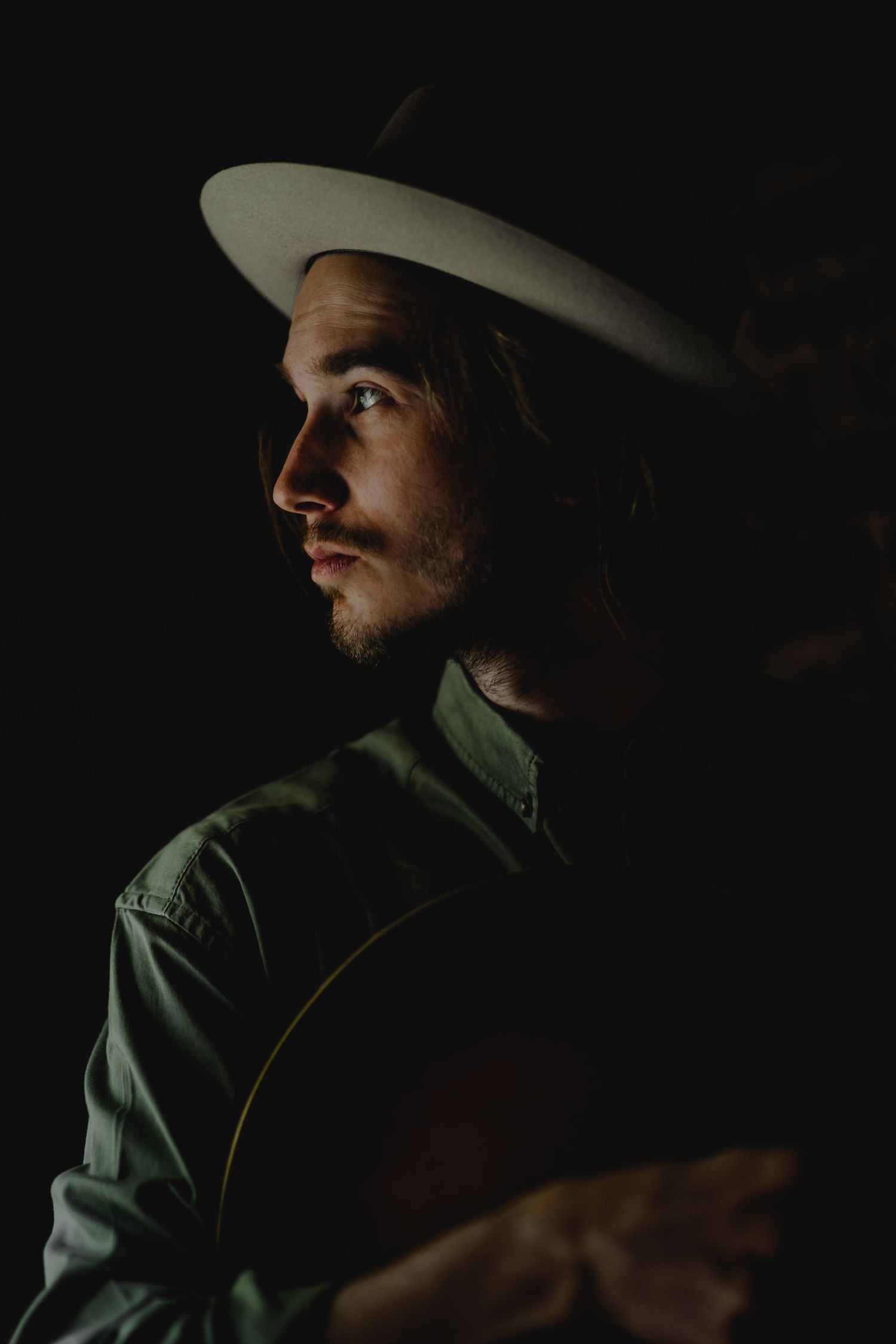 Dramatic low-light portrait series showing a person in a cowboy hat and green shirt against dark shadows.