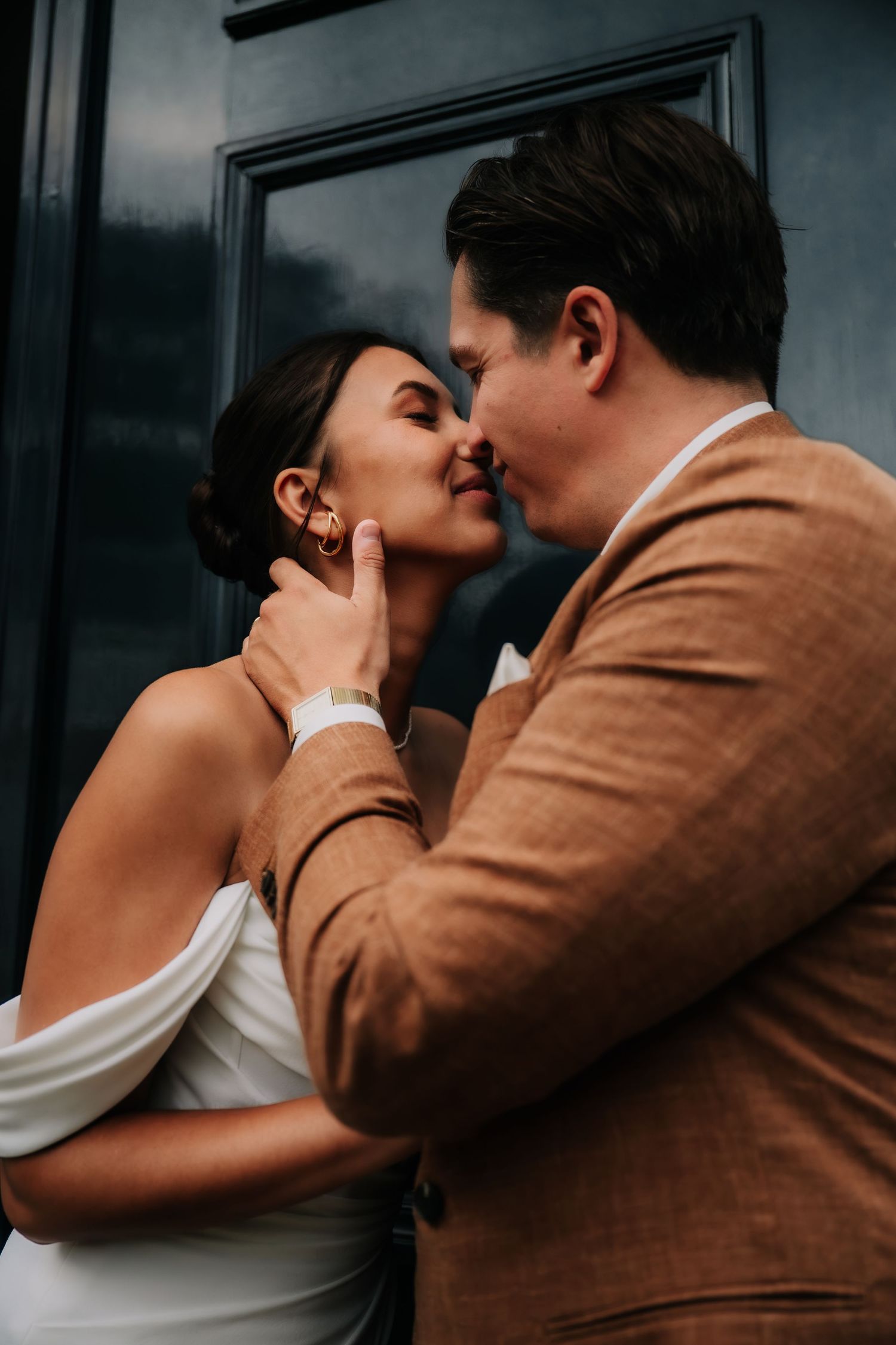 Romantic couple sharing an intimate moment, groom in brown suit tenderly cupping bride's face for a kiss.