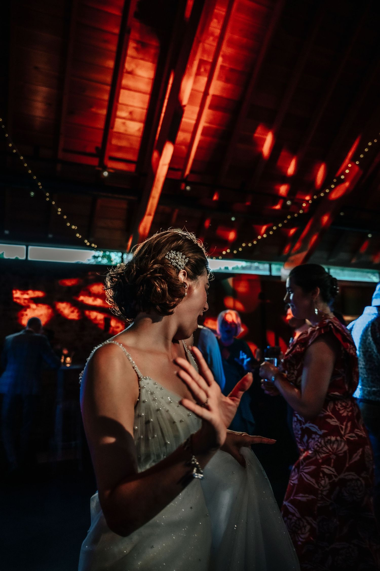A dimly lit wedding reception dance with red ambient lighting and string lights overhead.