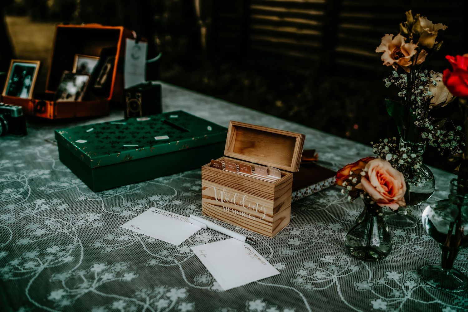 A rustic wooden box with vintage styling sits on a dark marble countertop with scattered flower petals.