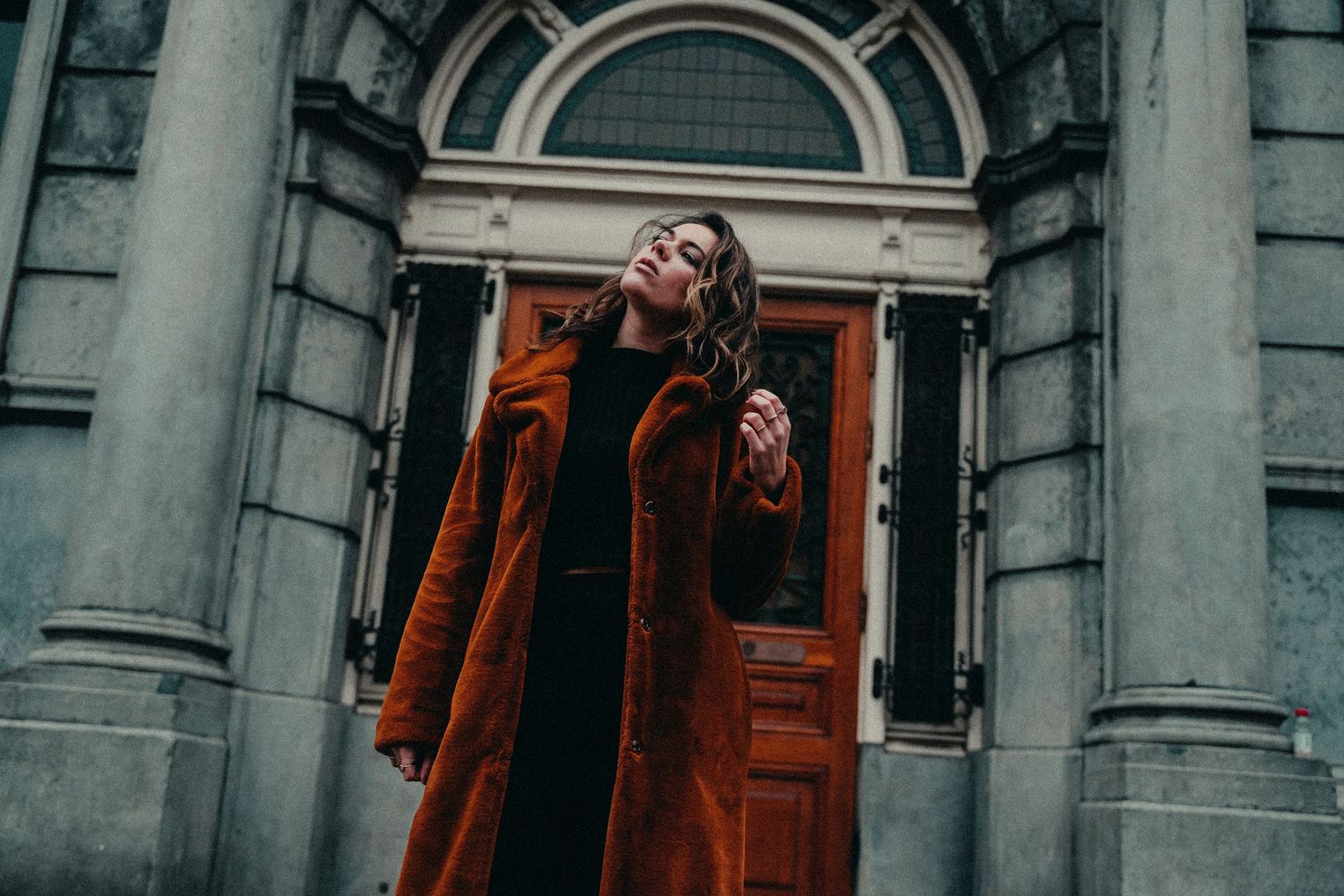 A grand stone building with ornate architectural details and red wooden doors stands against a moody gray sky.