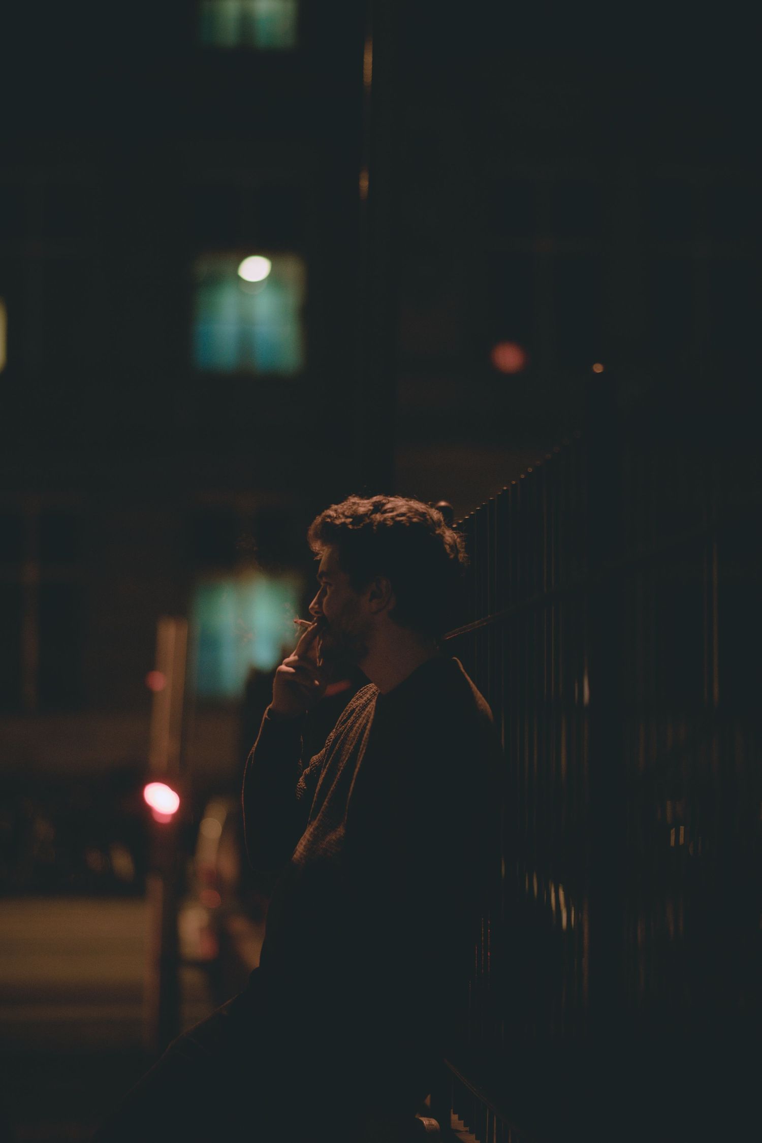 A dark and moody nighttime street scene with silhouettes against blurred city lights in the background.