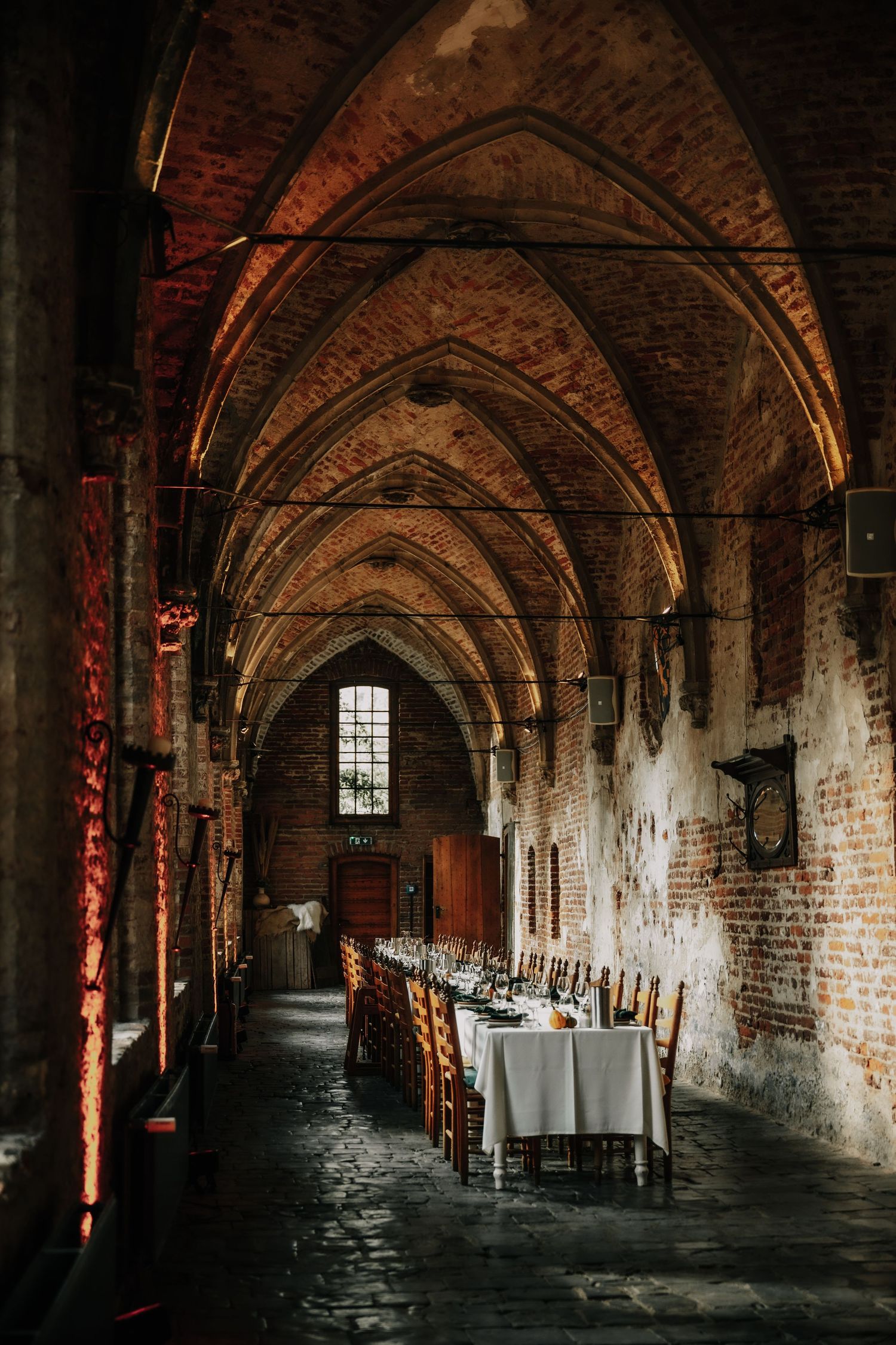 Atmospheric brick archway corridor with moody lighting and white-clothed tables set for dining in a historic venue.