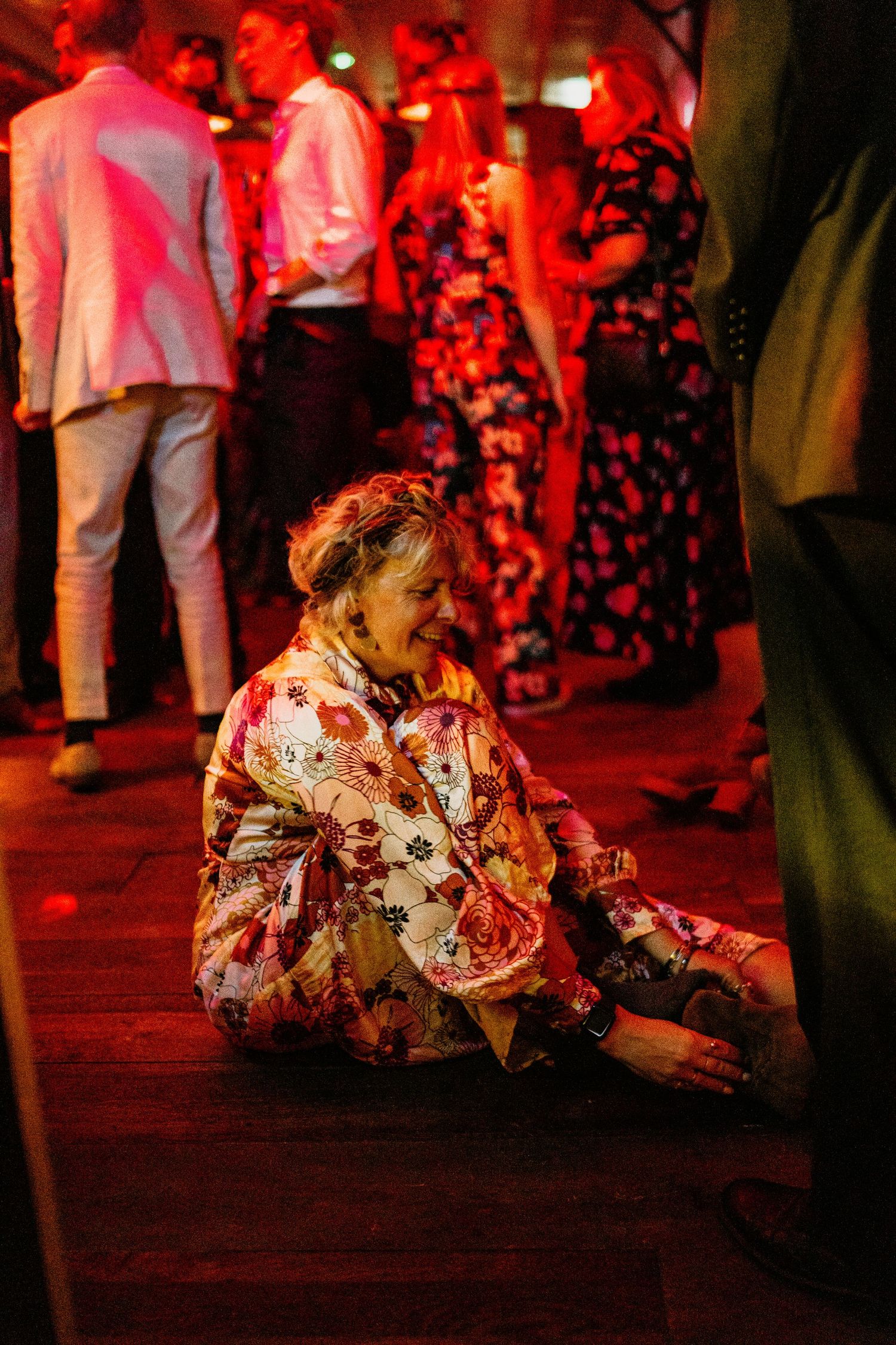 People in traditional dress dancing at a cultural celebration illuminated by dramatic red lighting.