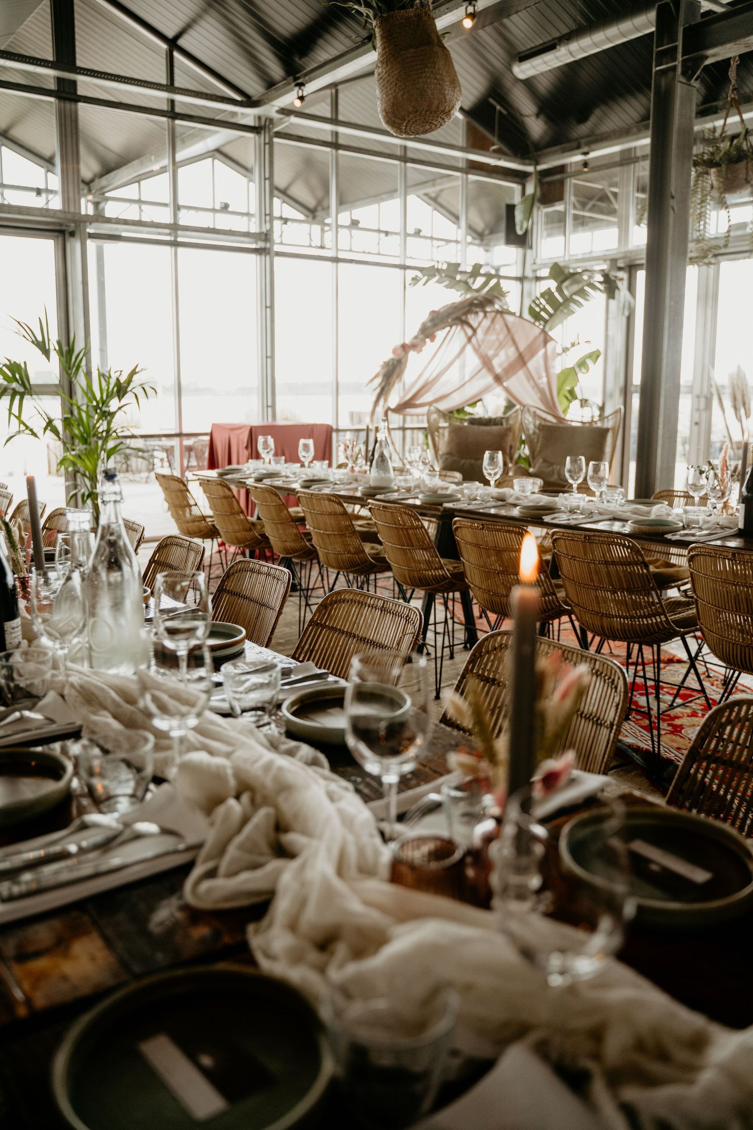 An elegant wedding reception setup with rattan chairs and tropical decor in a glass-walled venue.
