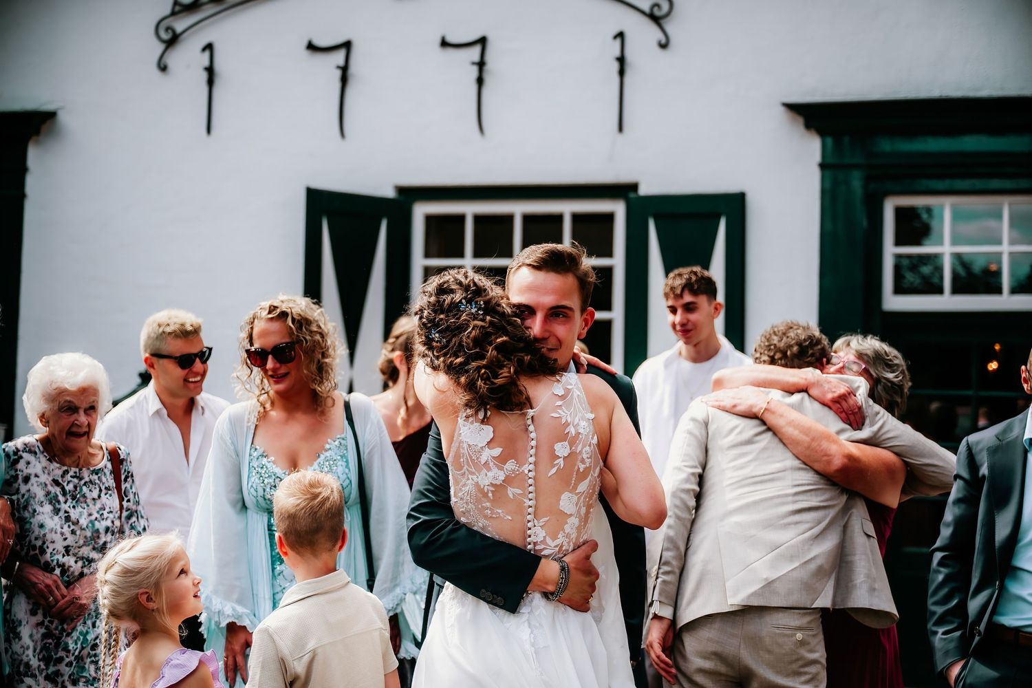 Wedding party celebrating outside traditional white building with black shutters.