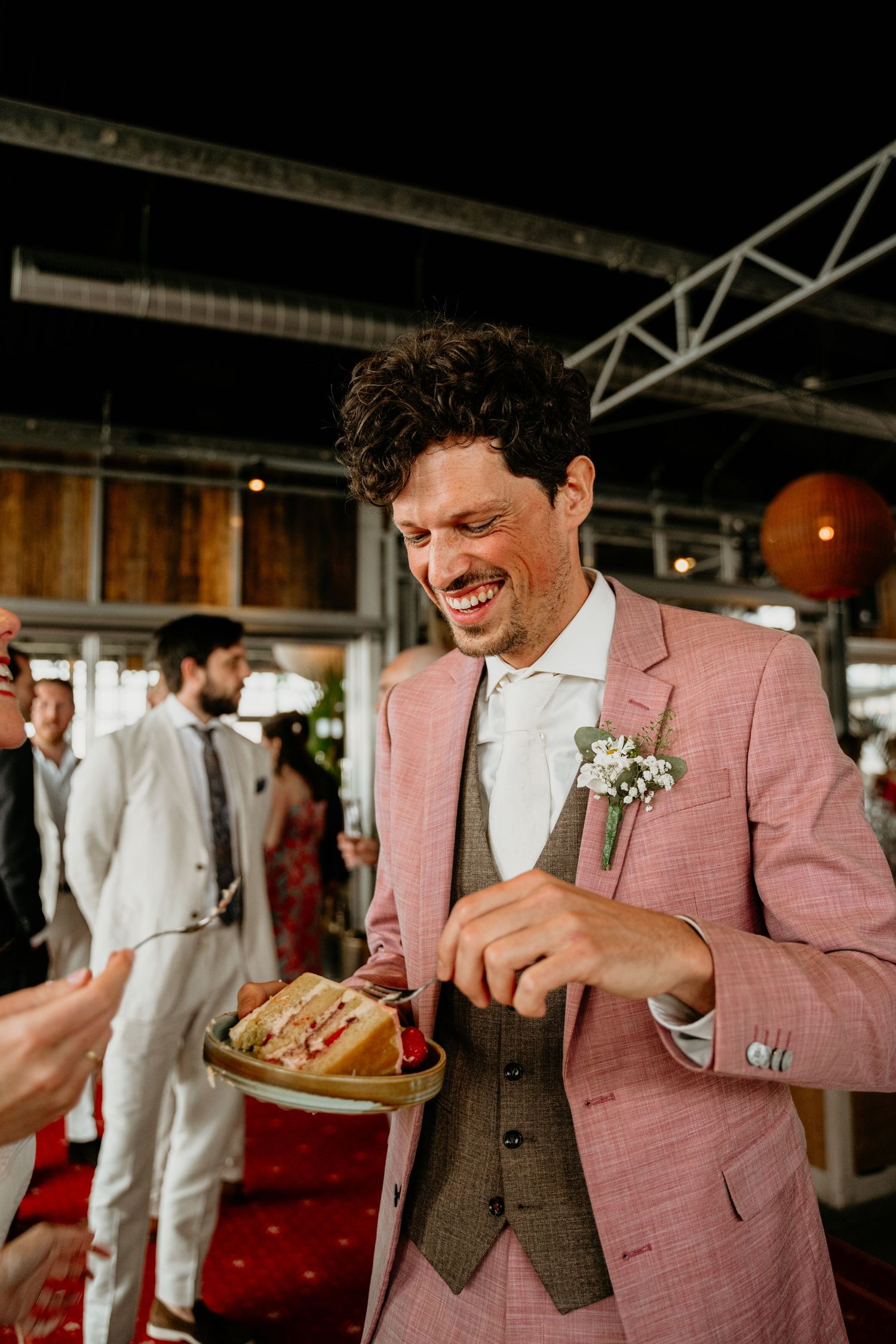 Person in pink suit jacket enjoying food at an indoor venue.