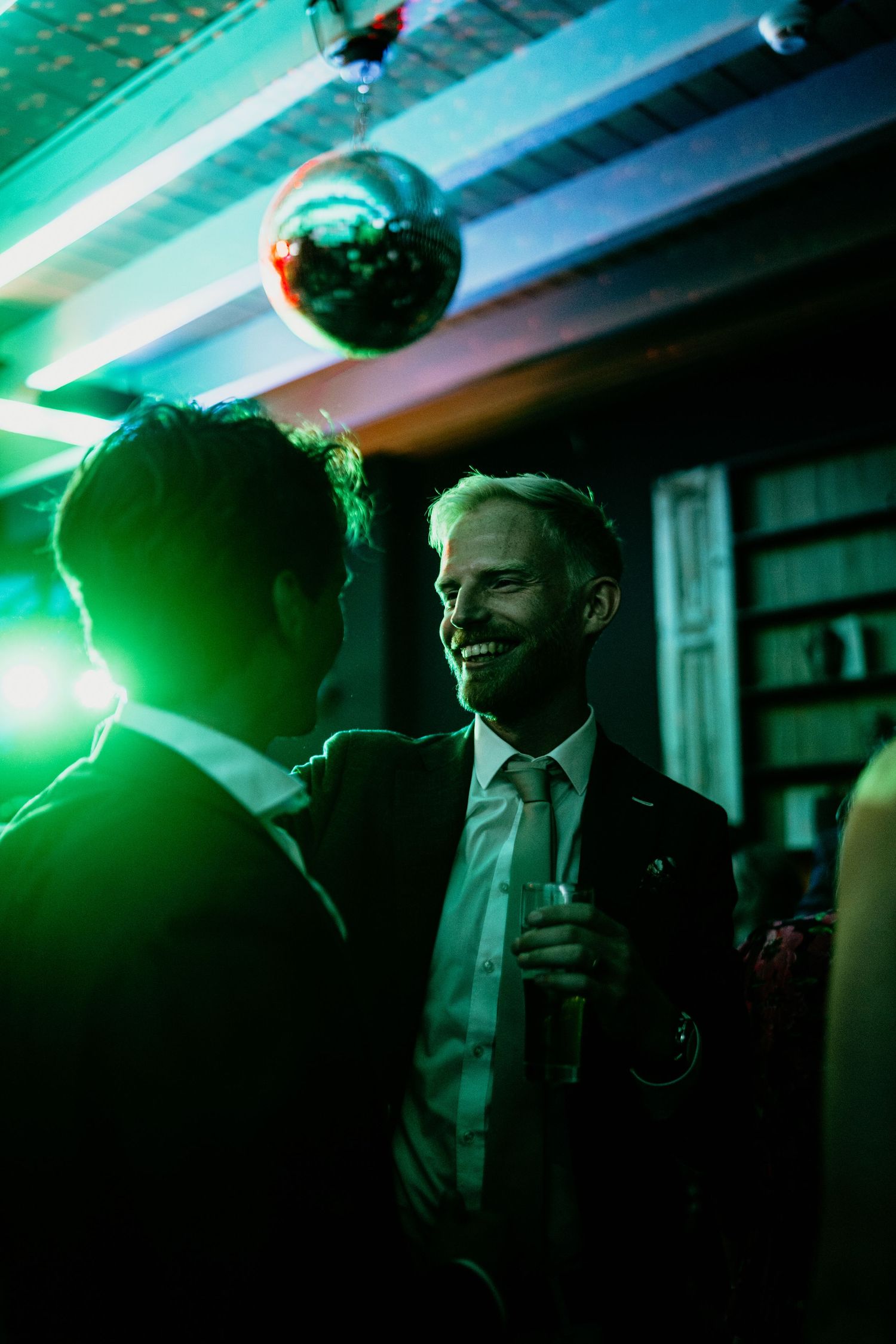 Wedding guests mingle under dramatic green lighting at an evening reception party.
