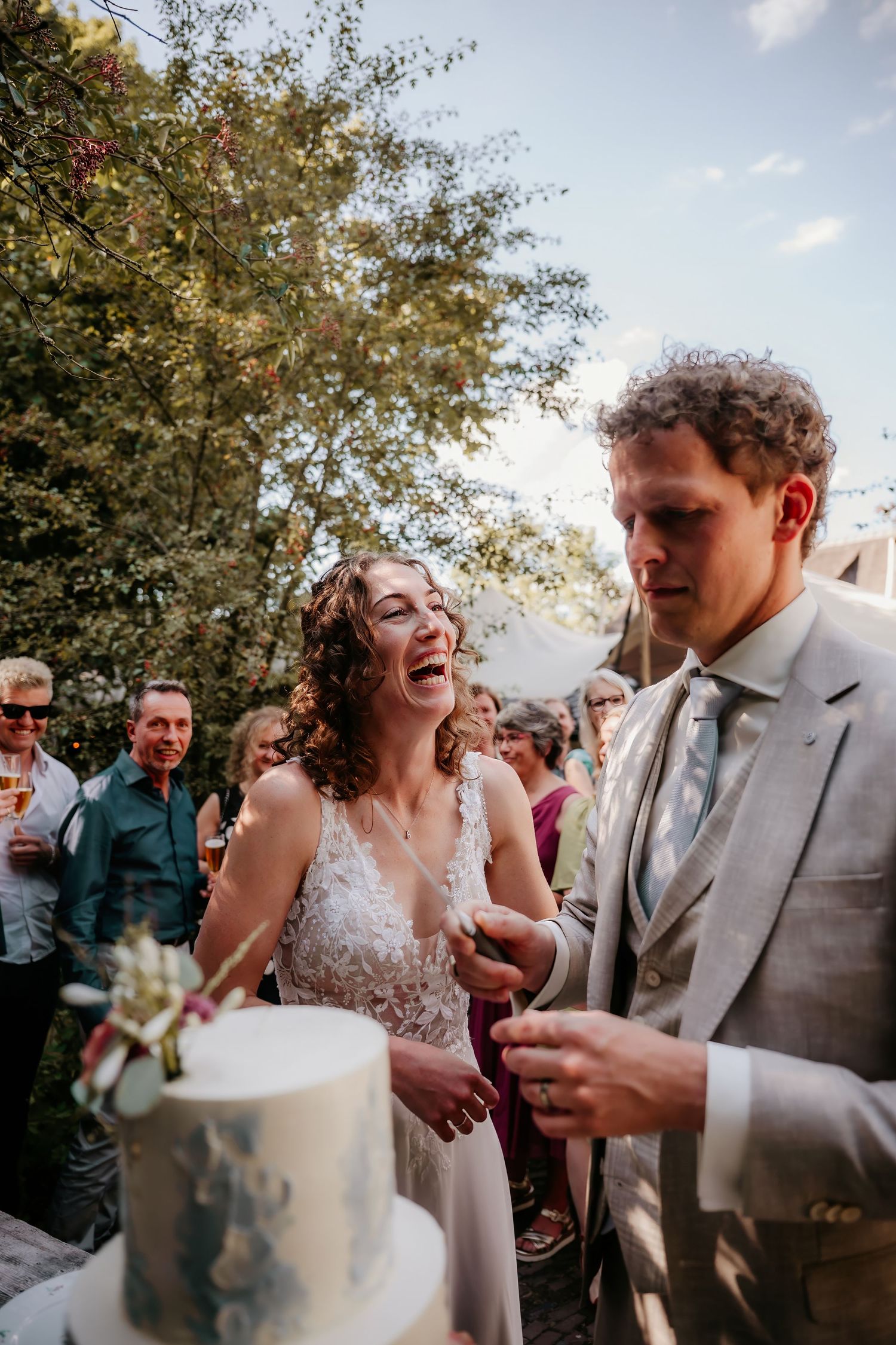 Newlyweds share a playful moment while cutting their white wedding cake at an outdoor reception.