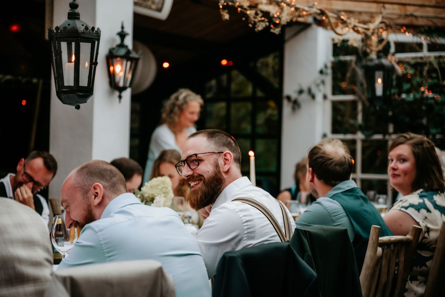 Wedding guests enjoying dinner at outdoor reception with vintage lantern lighting.