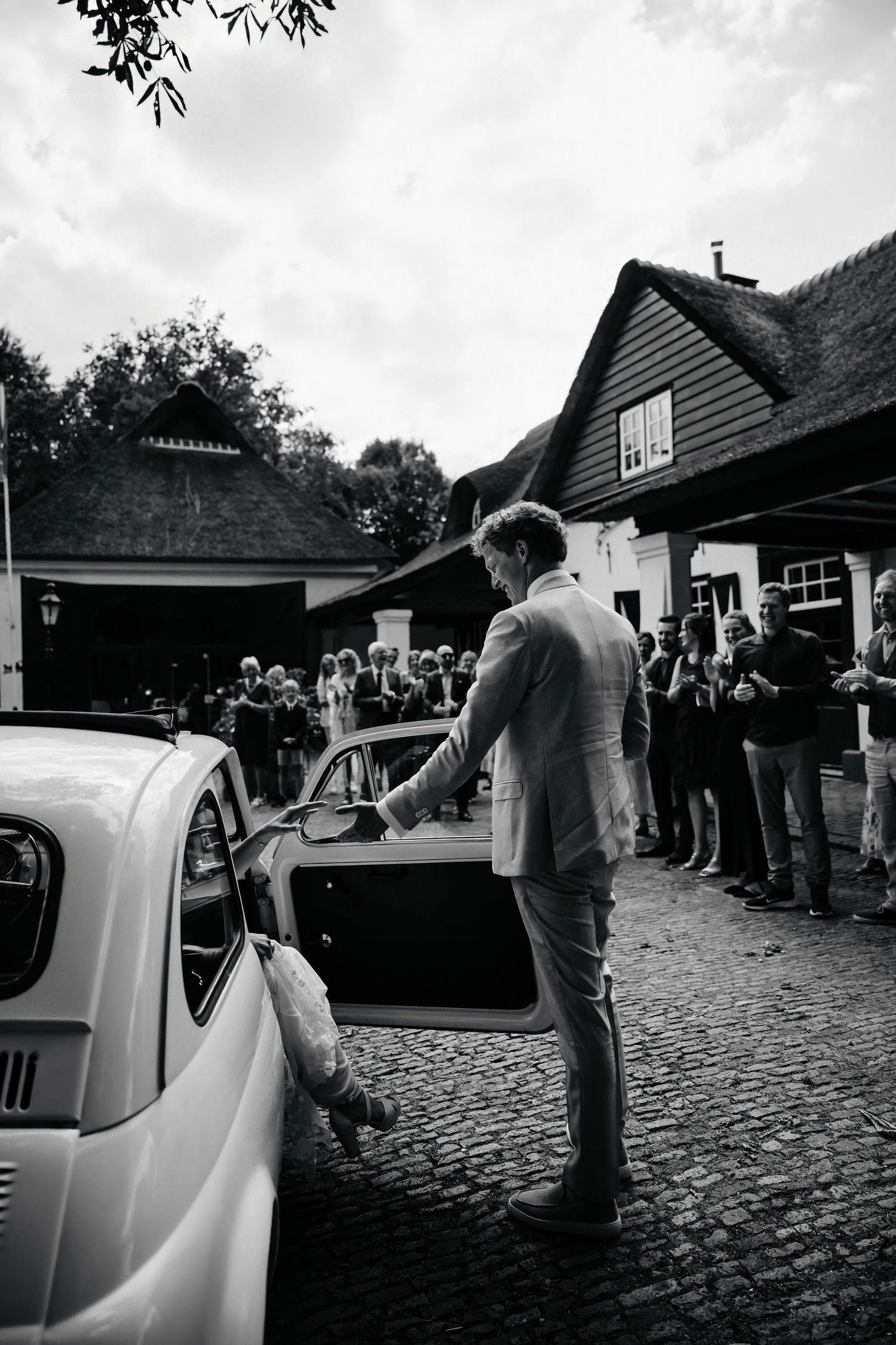Black and white photo of a vintage Volkswagen Beetle parked outside a rustic wedding venue.