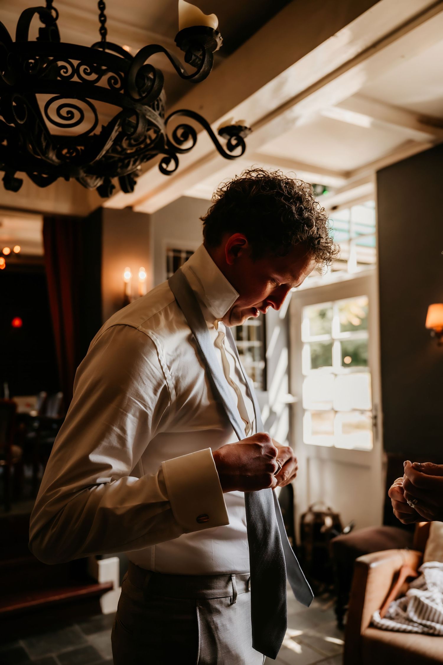 Person in white shirt preparing for formal event near ornate light fixtures.