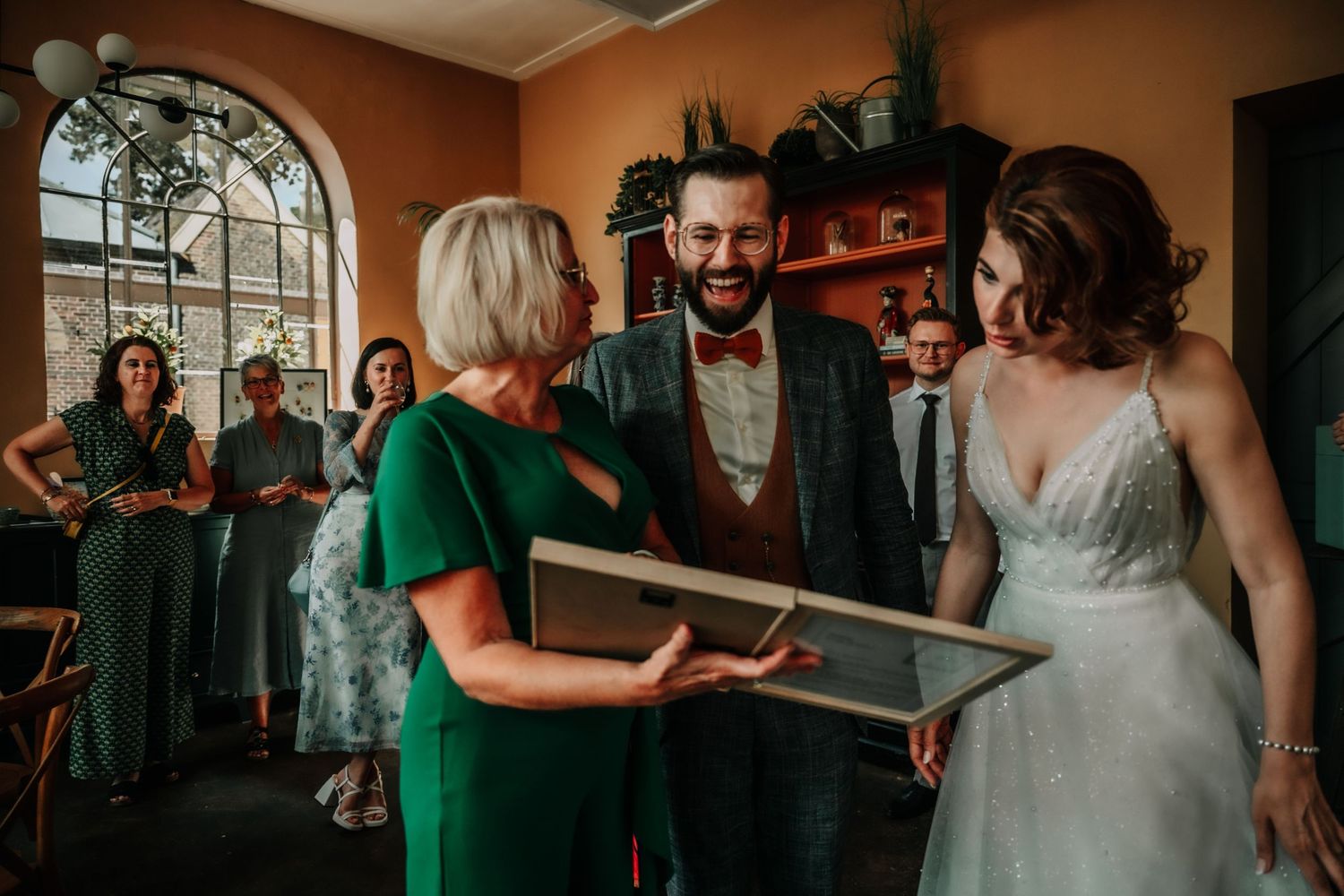 Wedding reception gathering in a warm-toned room with arched windows.