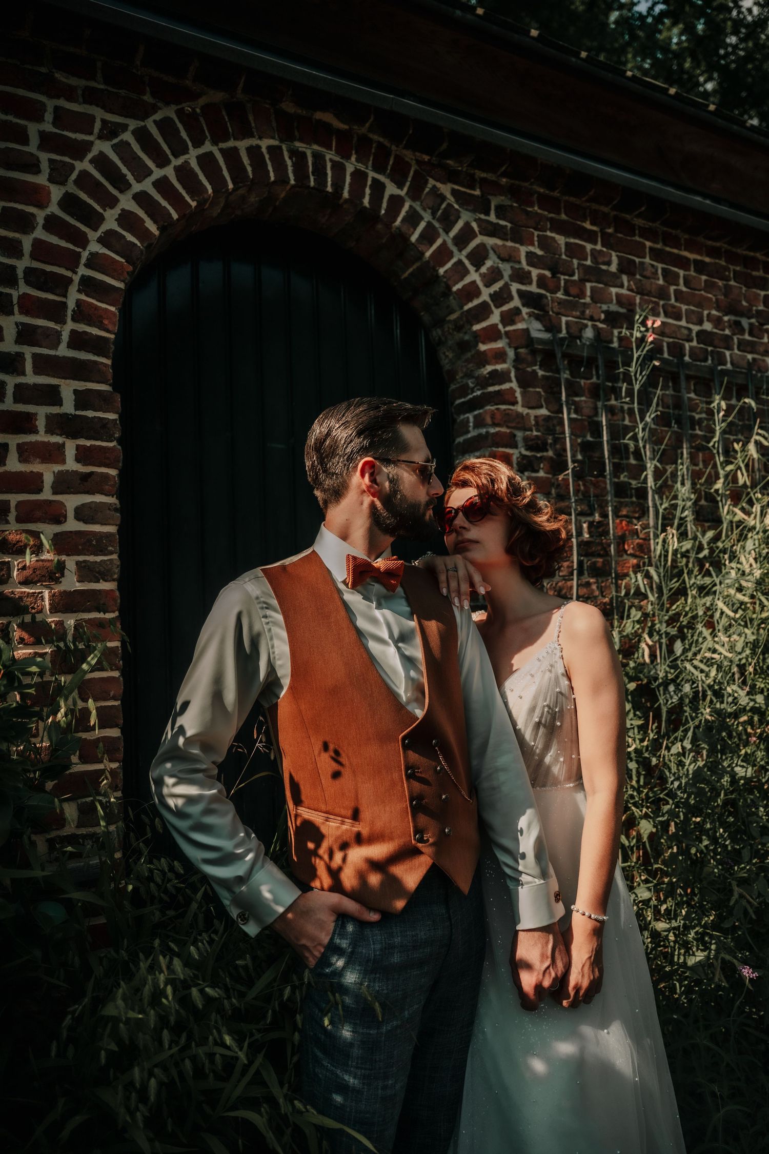 A tender embrace captured against weathered brick architecture and natural greenery.