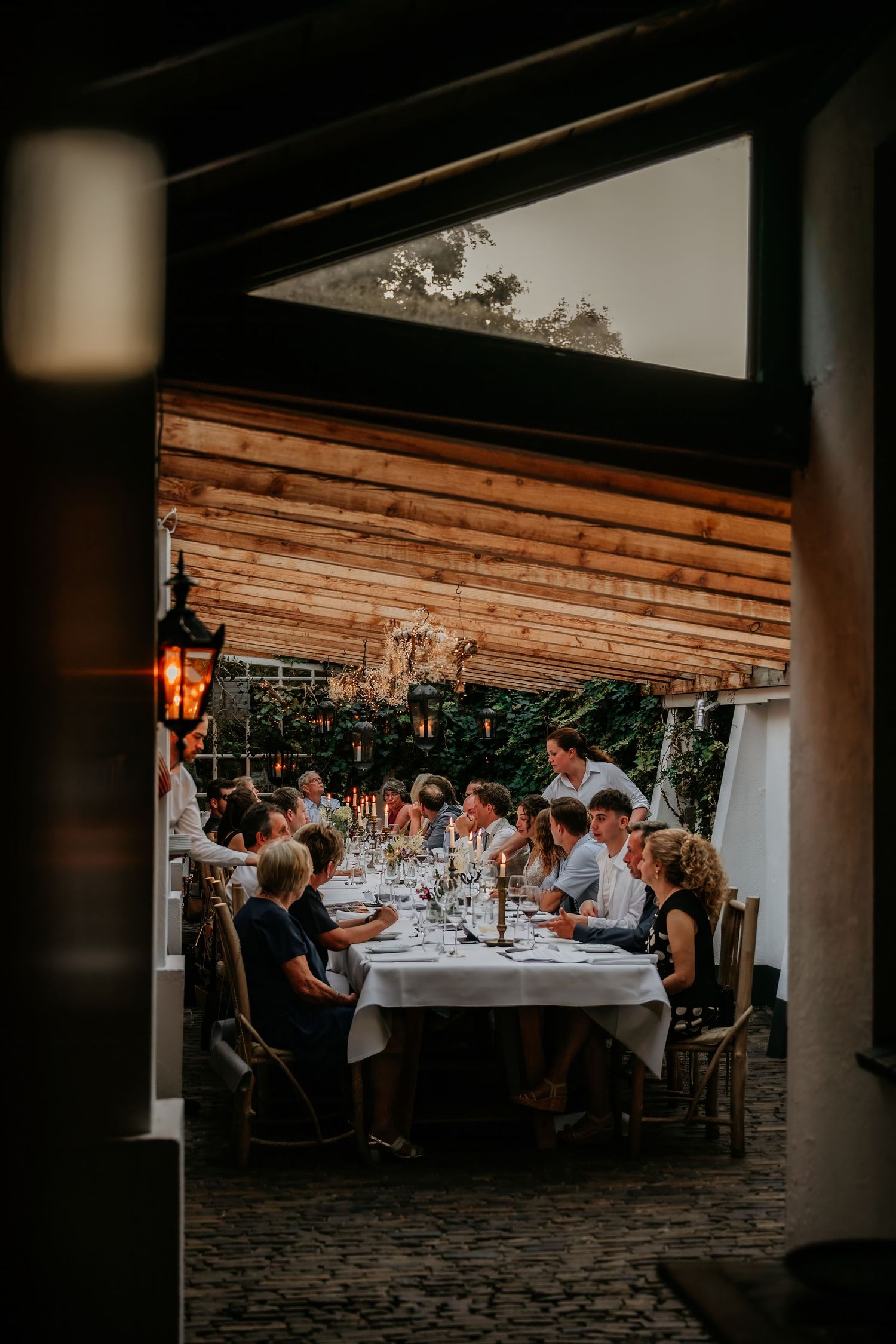 Wedding reception dinner setup under wooden beams with ambient lighting.