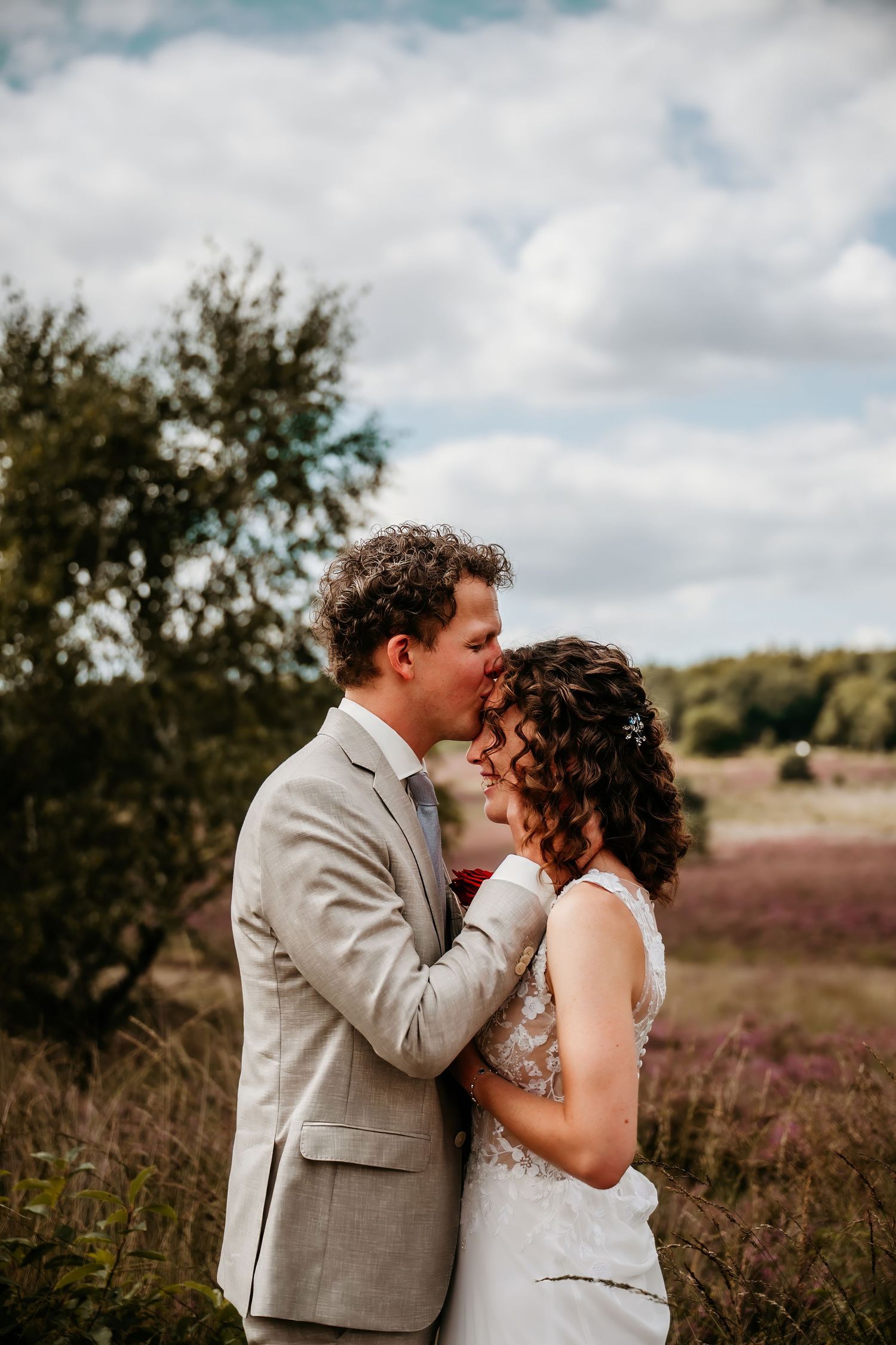 A romantic wedding moment captured in a field of purple heather under cloudy skies.