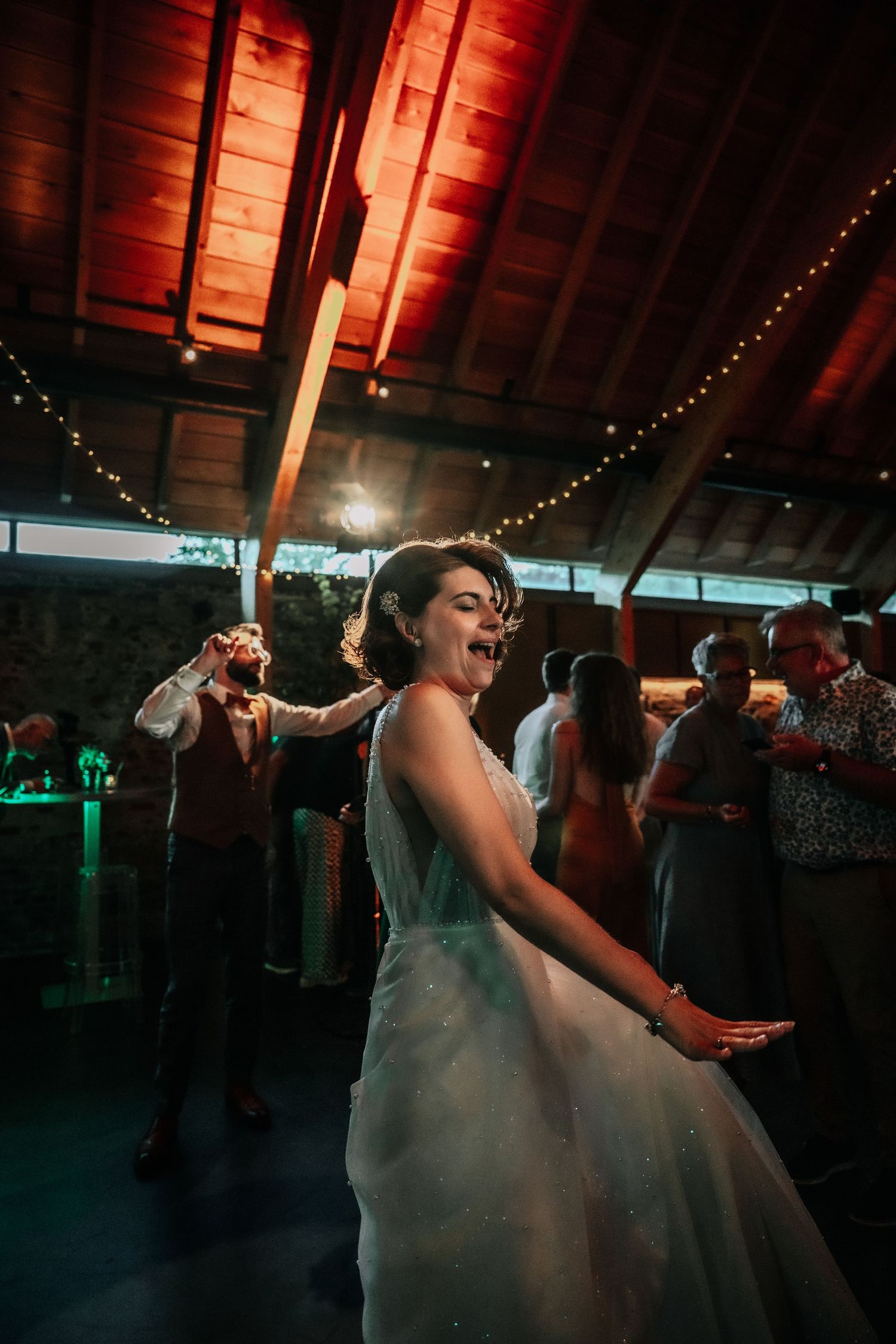 Wedding reception dance party in a rustic barn venue with string lights and red ambient lighting.