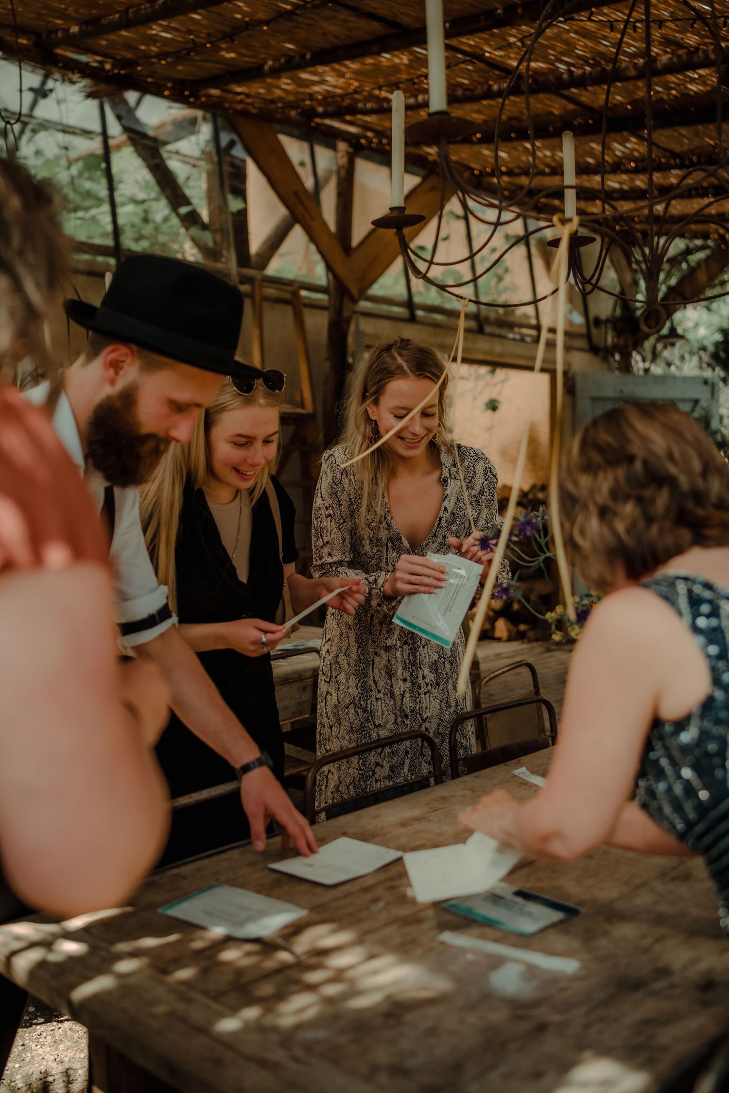 A group gathers around a rustic wooden table under a pergola examining papers in warm sunset lighting.