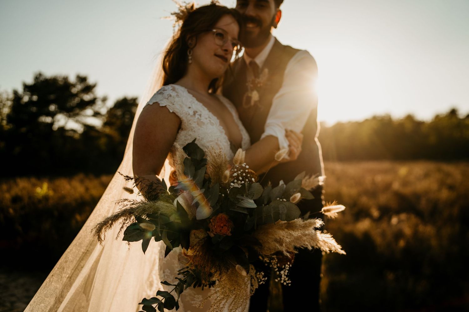Romantic sunset wedding portrait with couple embracing in warm evening light.