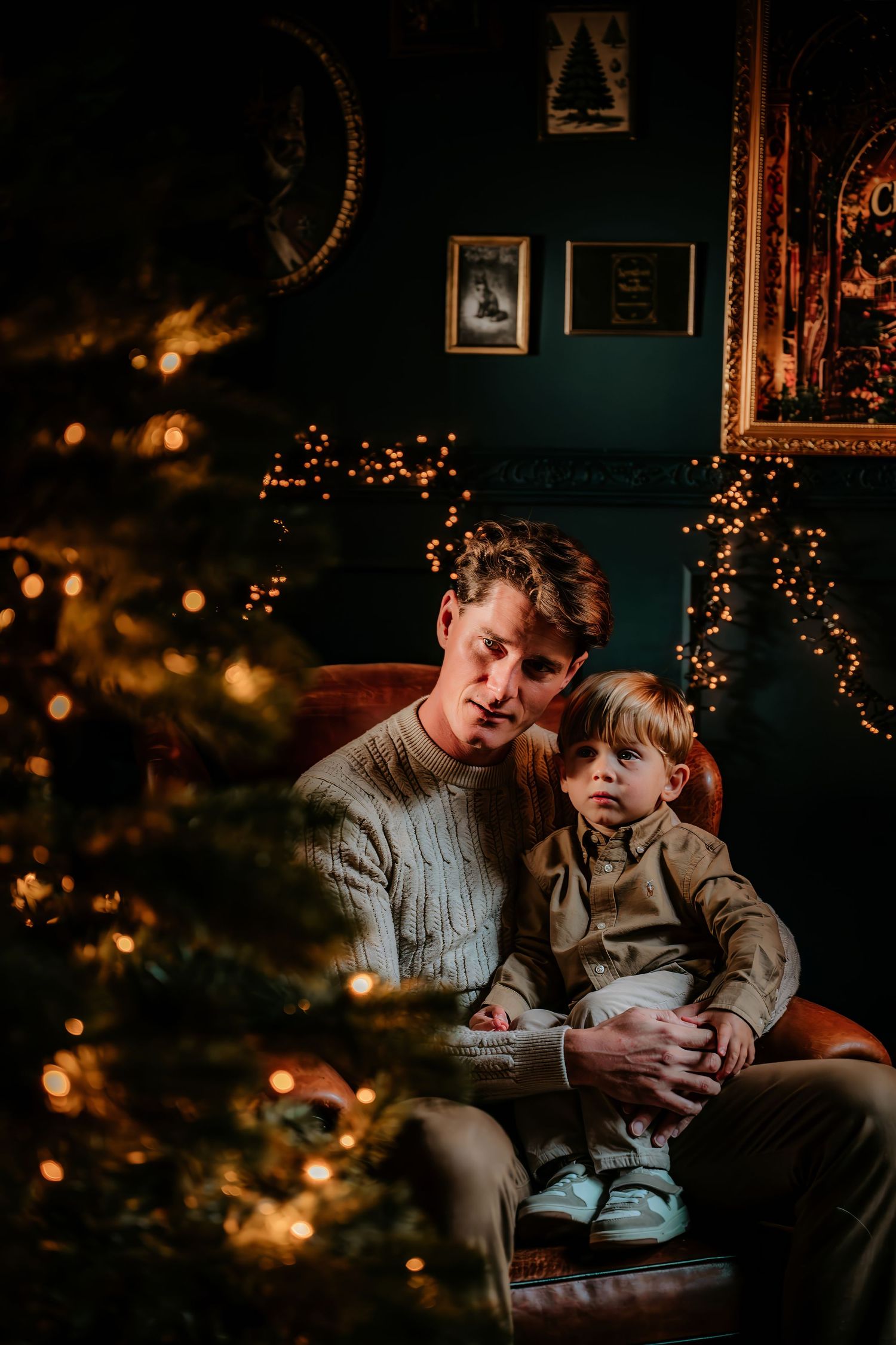 Family reading together by warm Christmas tree lights in cozy living room with dark teal walls.