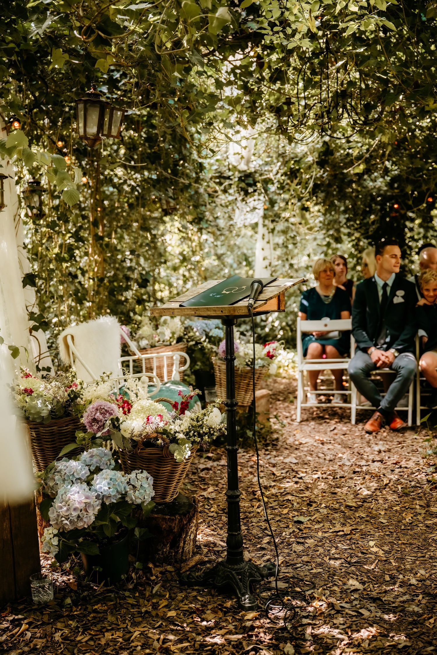 Garden wedding ceremony setup with floral arrangements and lanterns under leafy trees.