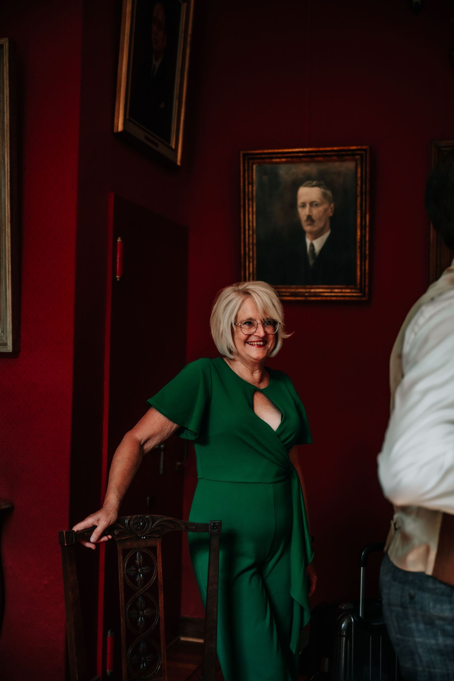 Person in emerald green dress smiling and gesturing in a room with red walls.