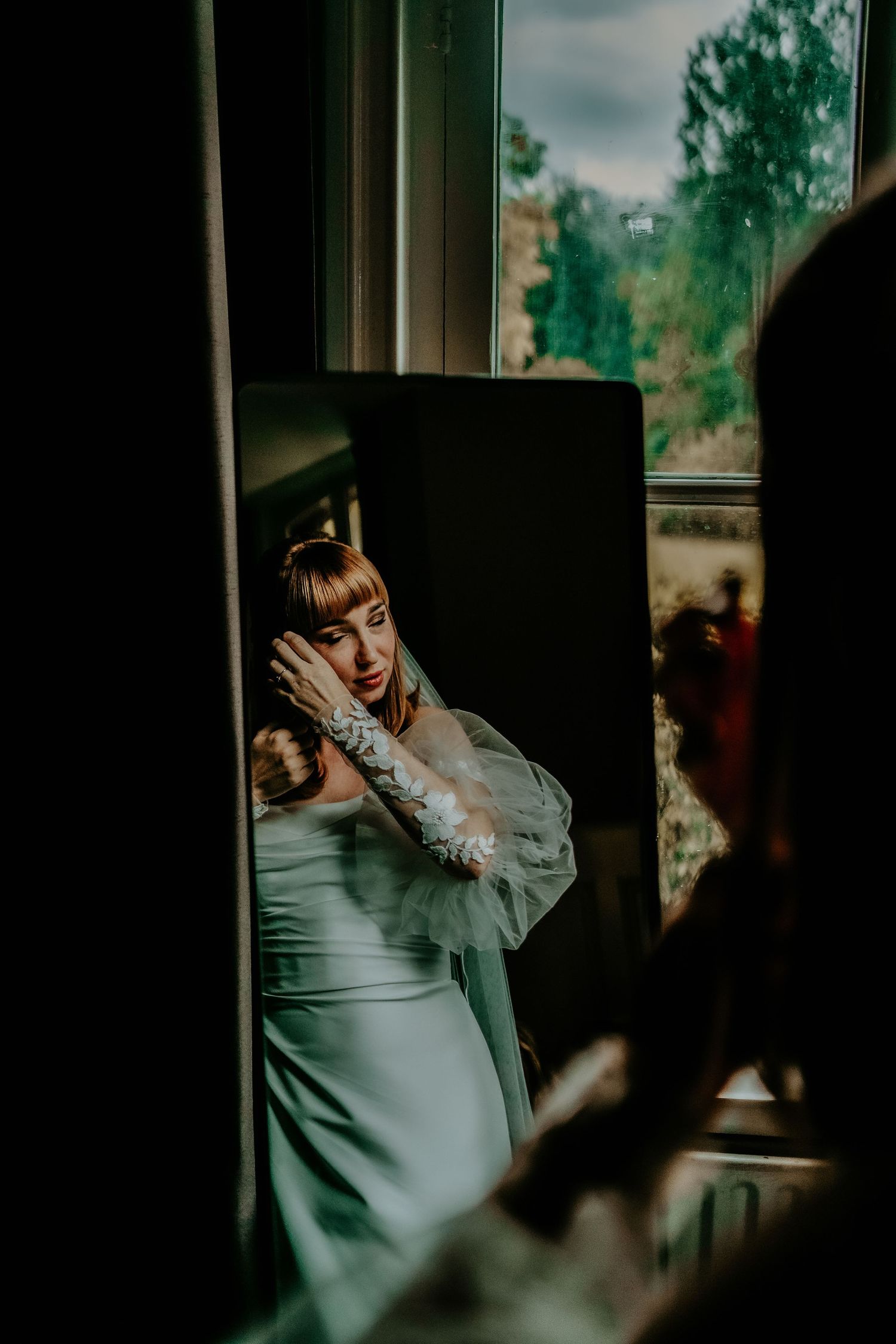 A person in a white dress is captured through a window reflection with dramatic lighting.