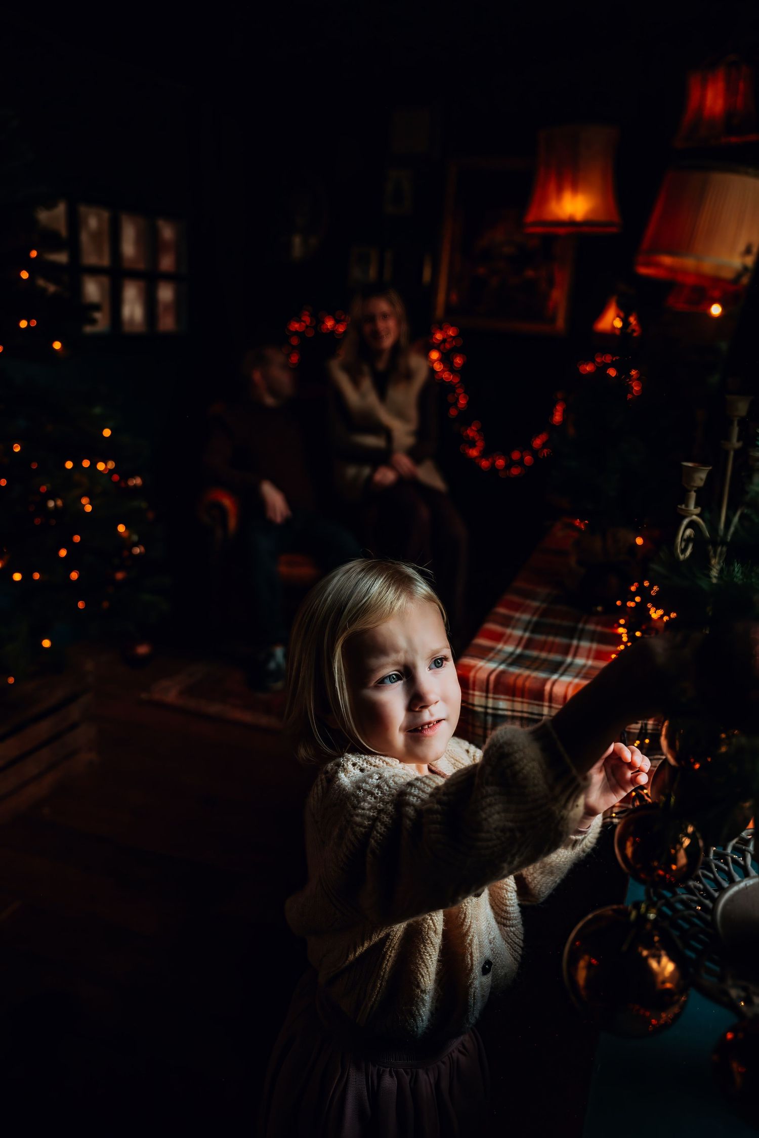 A child gazes at holiday decorations in a cozy room illuminated by warm Christmas lights.