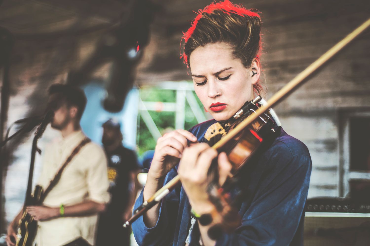 Musicians perform together on stage with violins and other string instruments during a live concert performance.