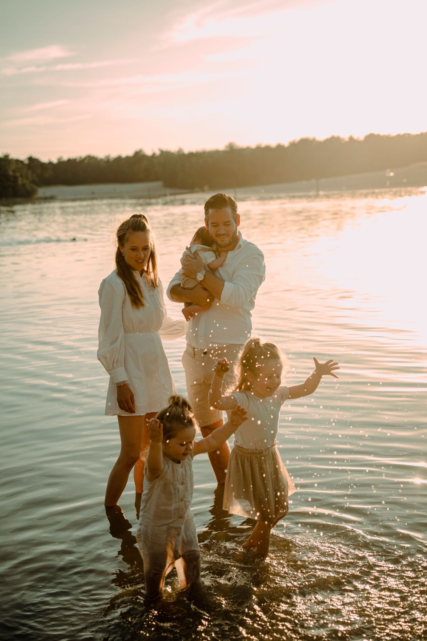 A family plays and splashes together at sunset in a lake, creating a joyful summer moment by the water's edge.