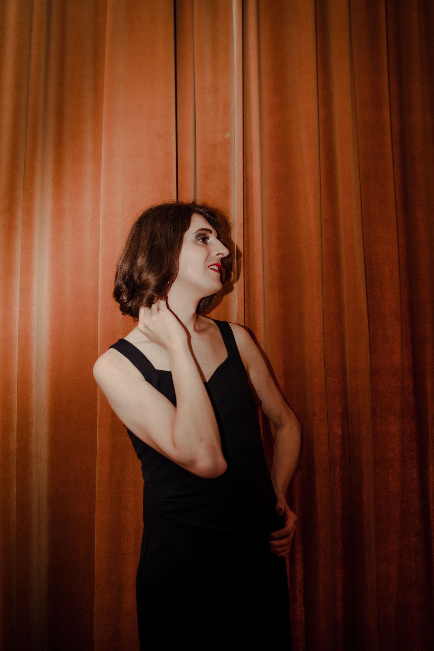 A person in a black top poses expressively against a brown curtain backdrop in a sequence of artistic shots.
