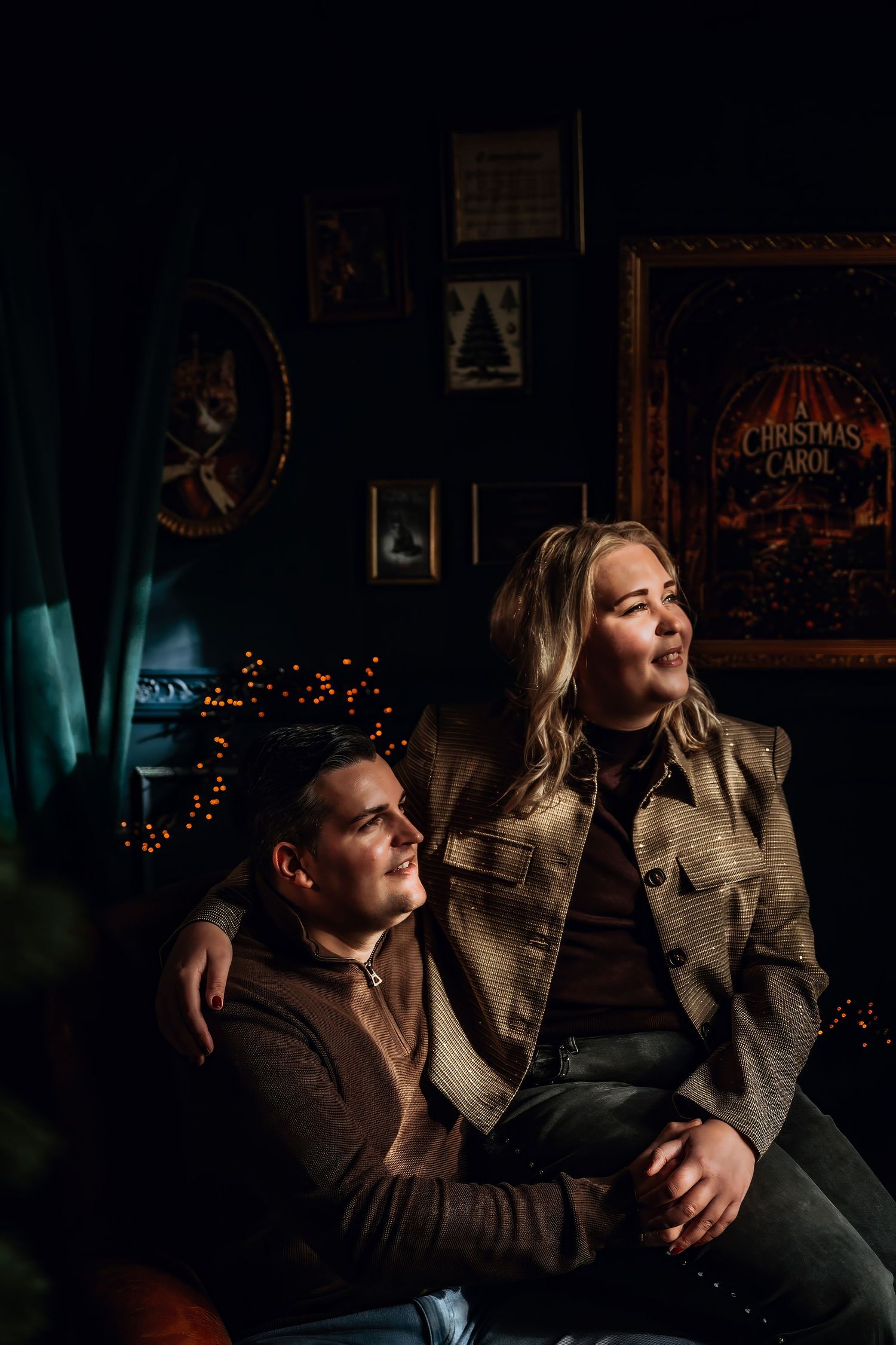 Couple shares intimate moment on couch with warm Christmas lights glowing in dark room.
