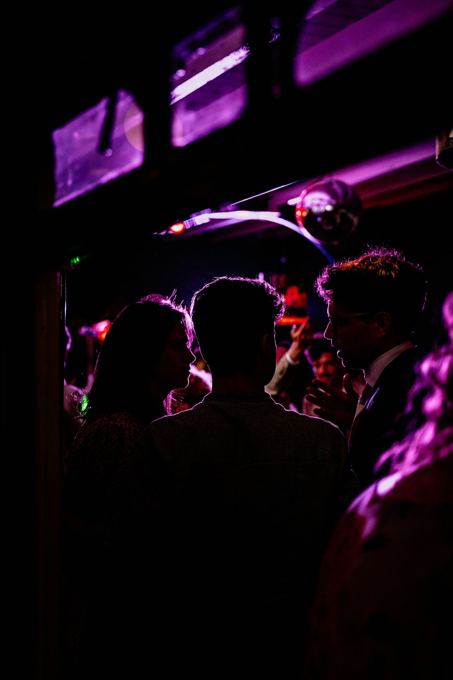 Silhouettes of people dancing in a dark nightclub with purple and red lighting effects creating a moody atmosphere.