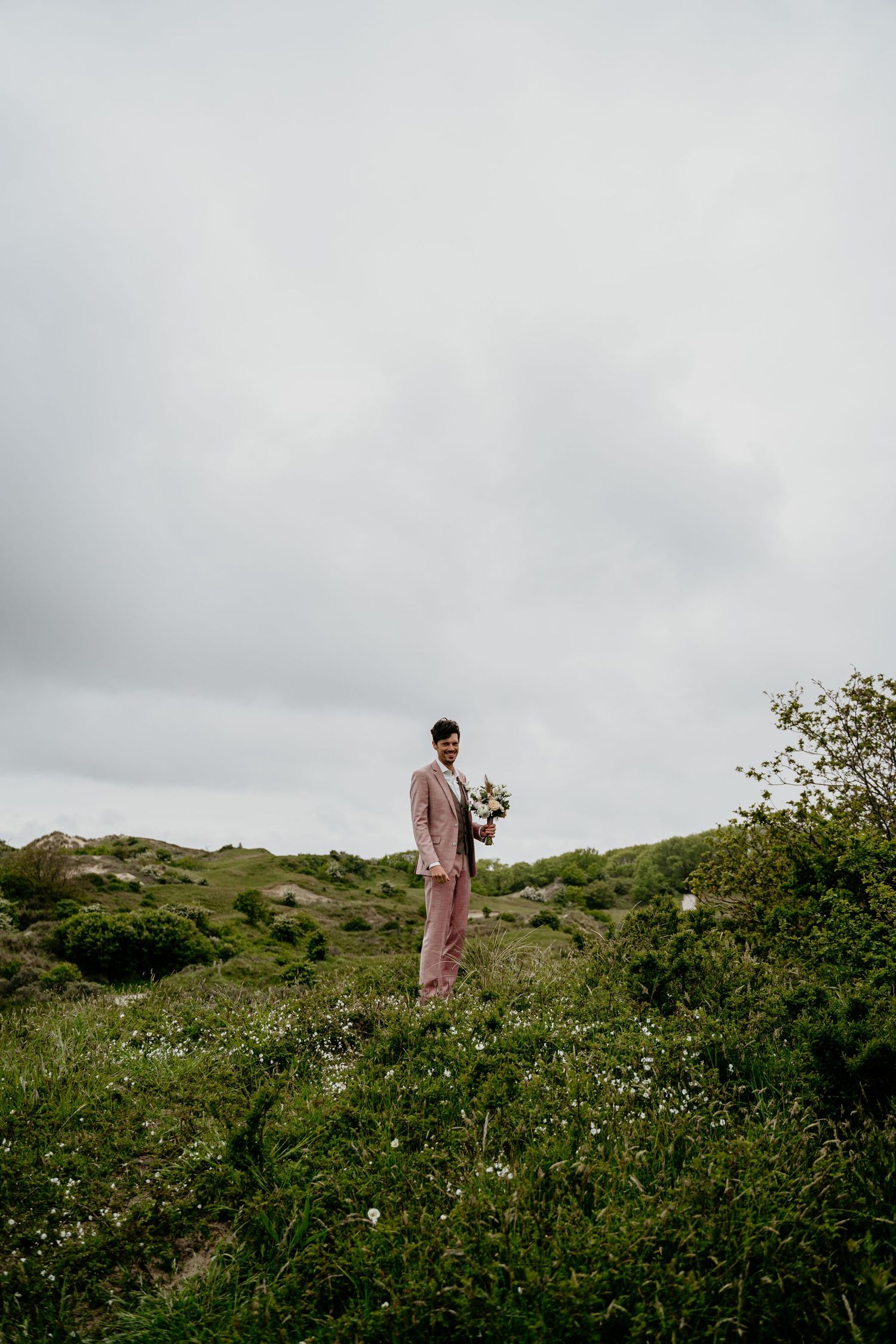 A person in pink stands on a grassy hillside against an overcast sky.