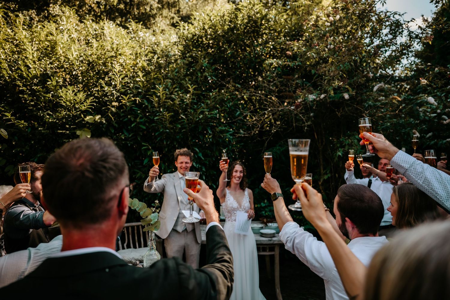Wedding guests raise their glasses in celebration during an outdoor reception at sunset.