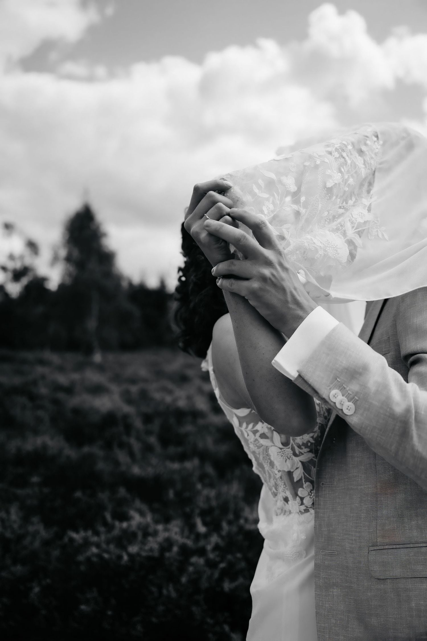Black and white close-up of clasped hands in wedding attire showing intimate connection.