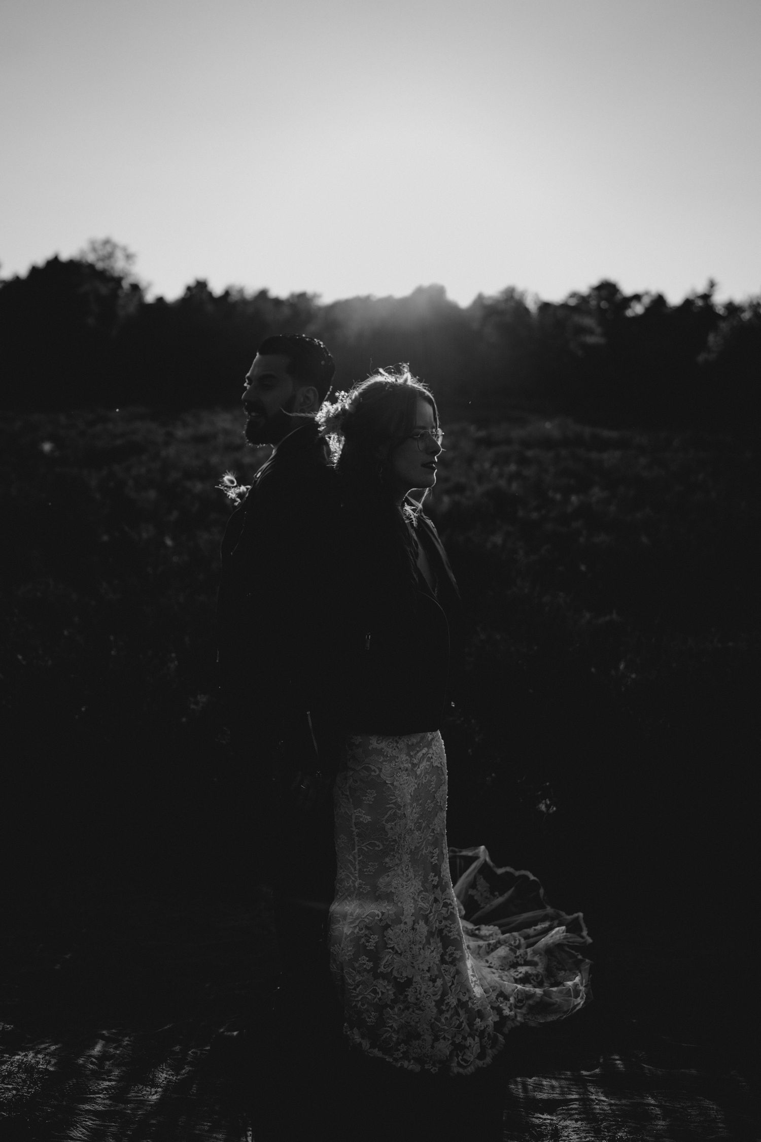 A silhouetted figure stands in a field at sunset creating a dramatic black and white portrait.