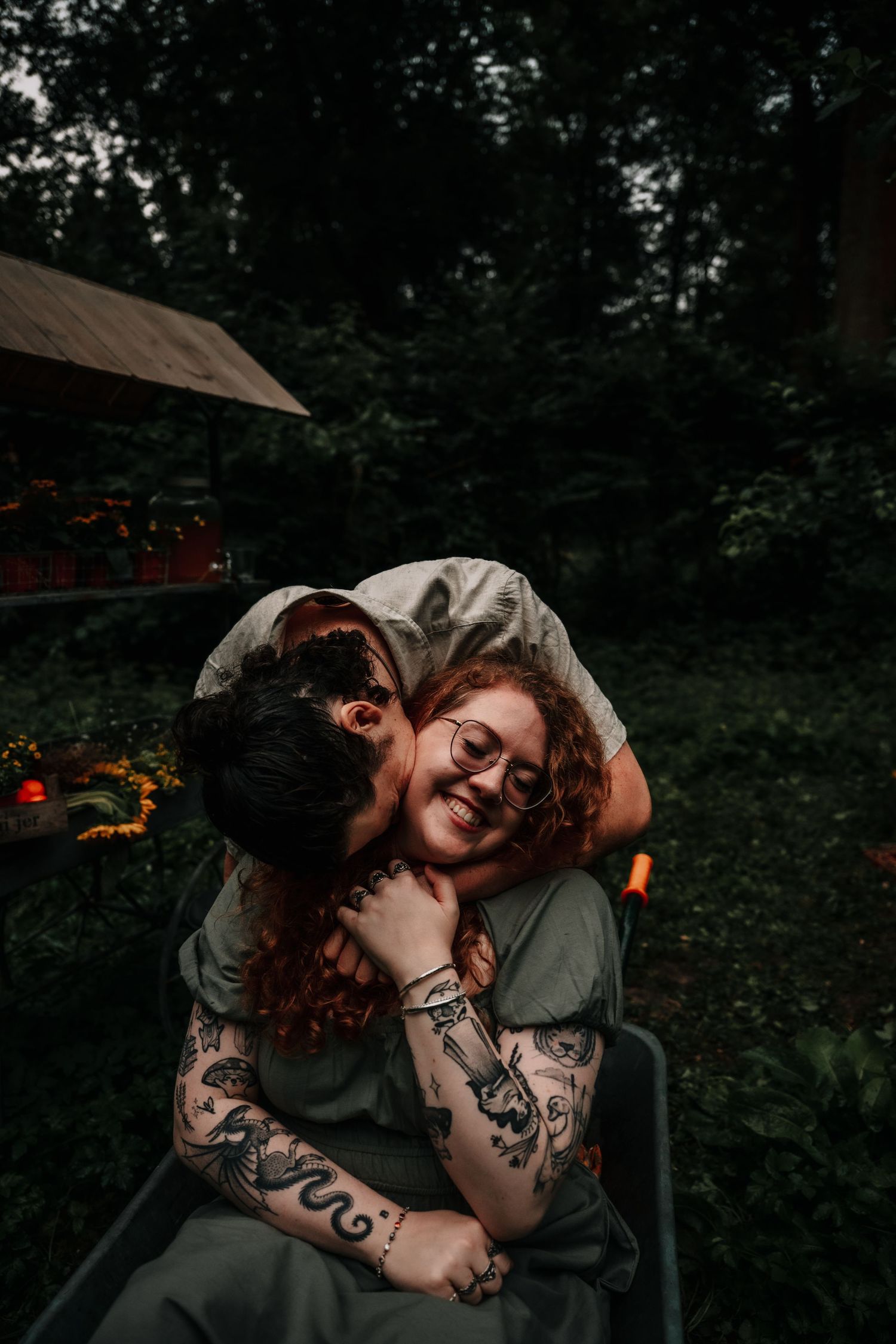 A couple shares an intimate moment together in a dark outdoor setting with trees visible in the background.