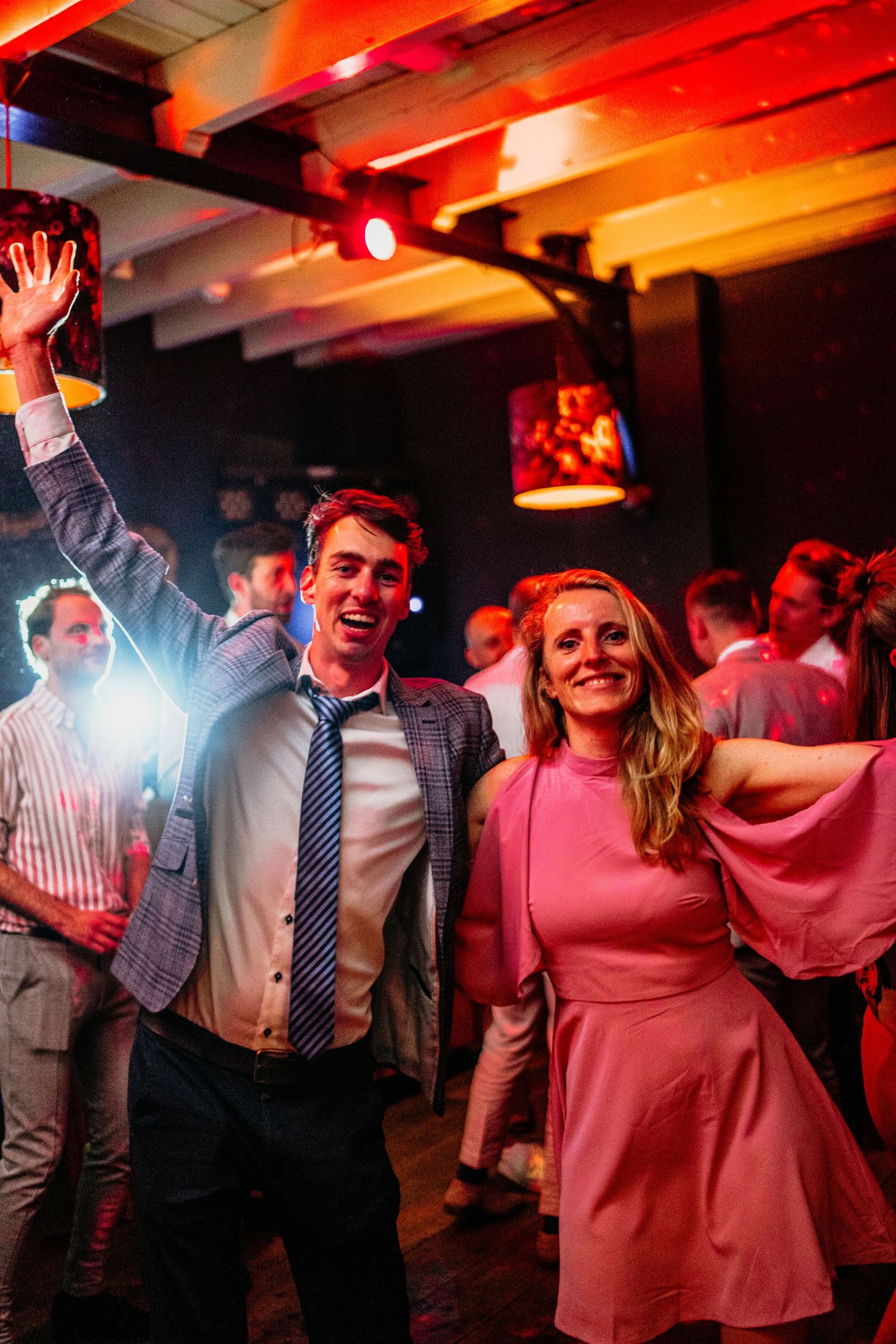 People dancing and celebrating at a lively indoor party with red ambient lighting.