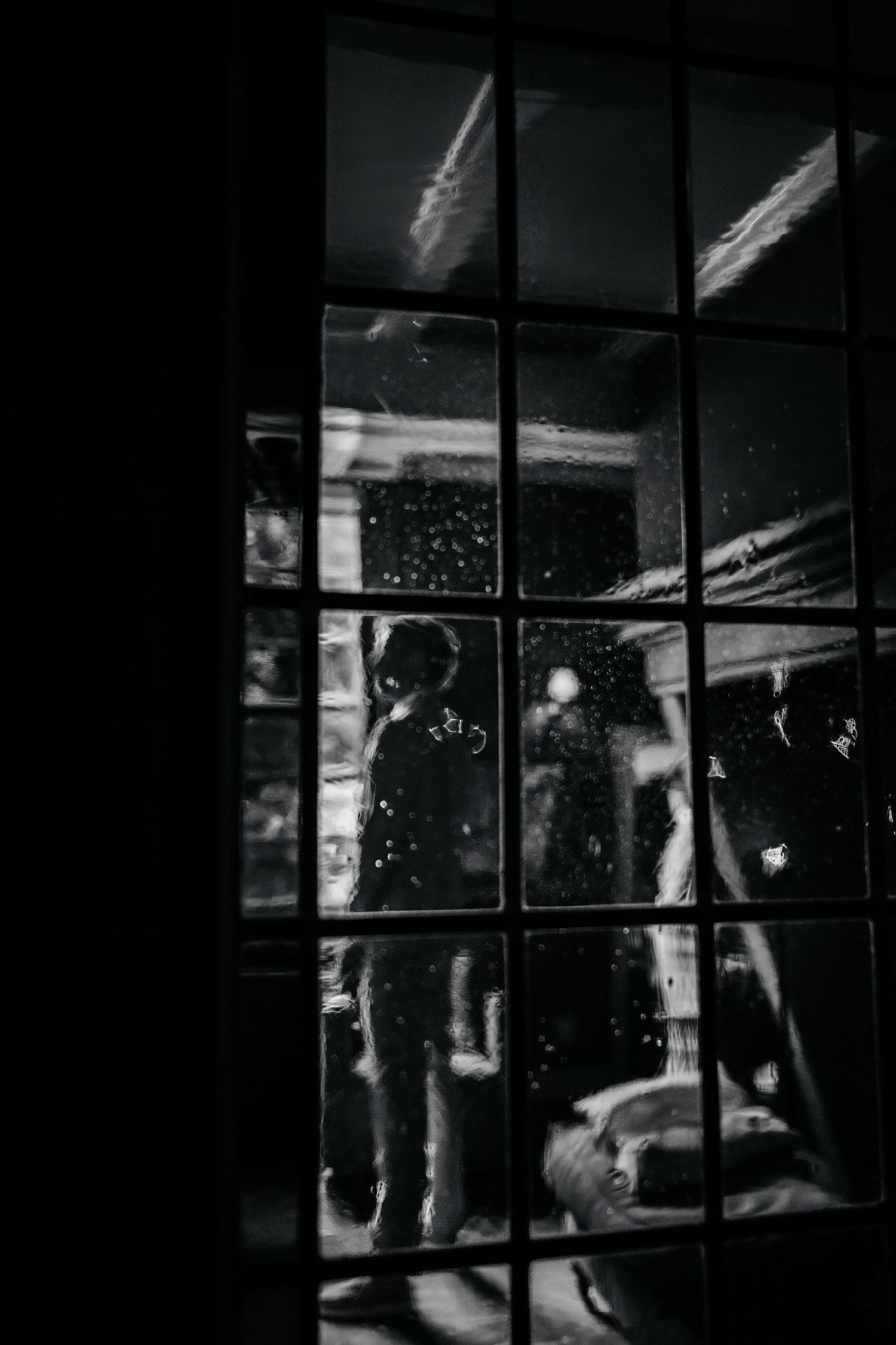 Silhouettes of figures seen through a window pane at night creating a moody atmospheric scene.