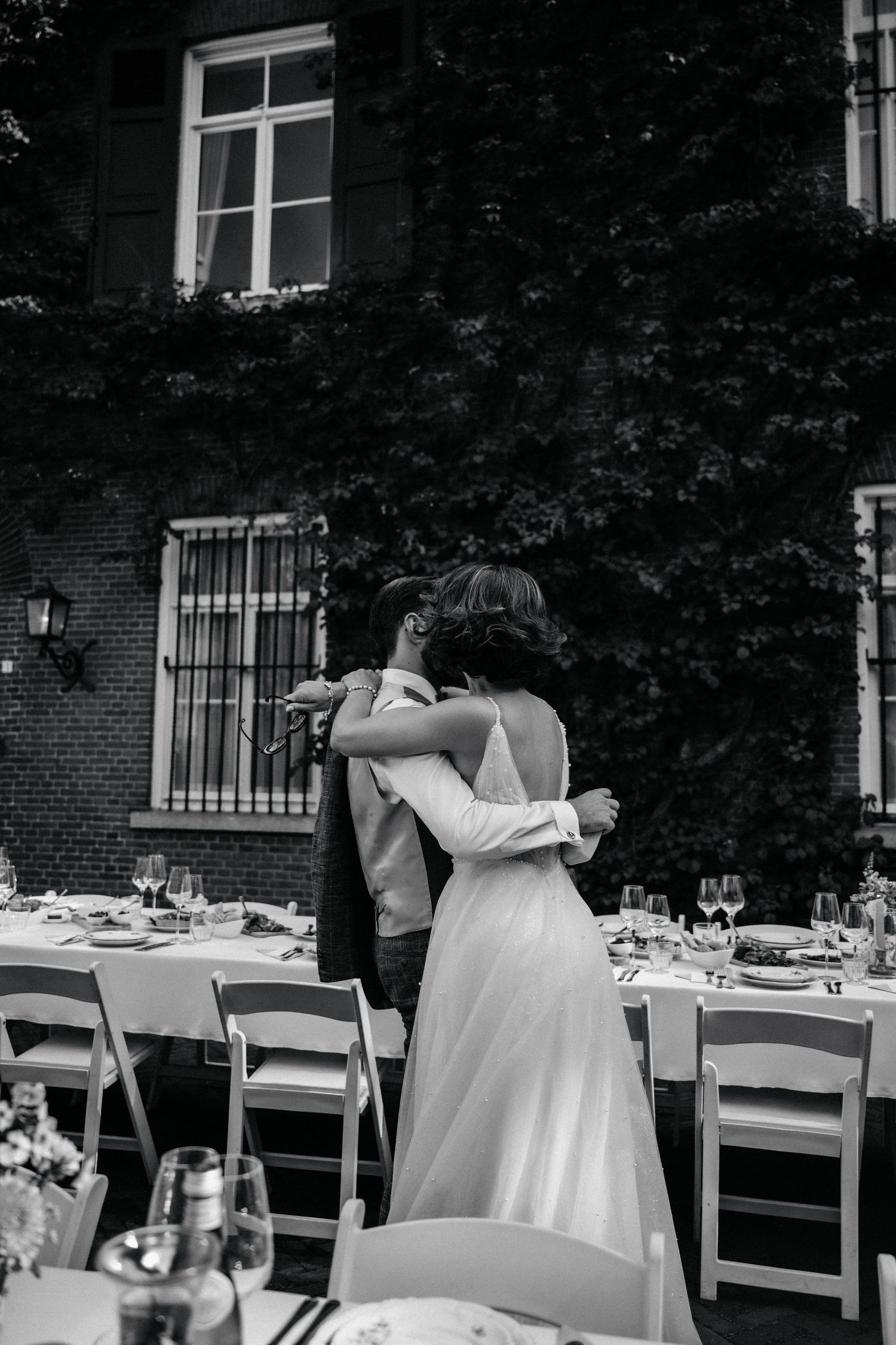 Wedding reception setup with white chairs and tables in an outdoor garden setting.