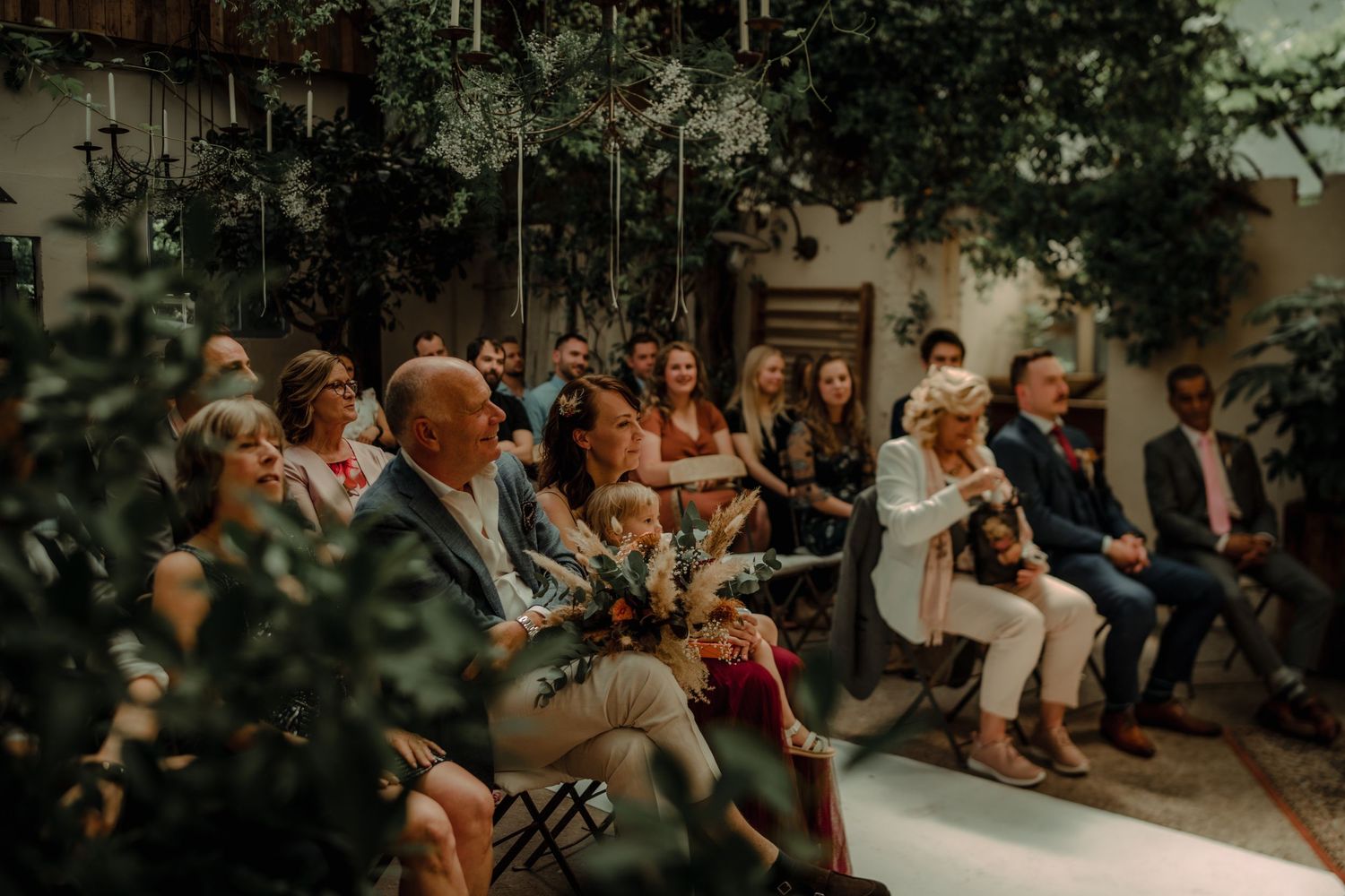 Wedding guests seated in rows under leafy branches during an outdoor ceremony.