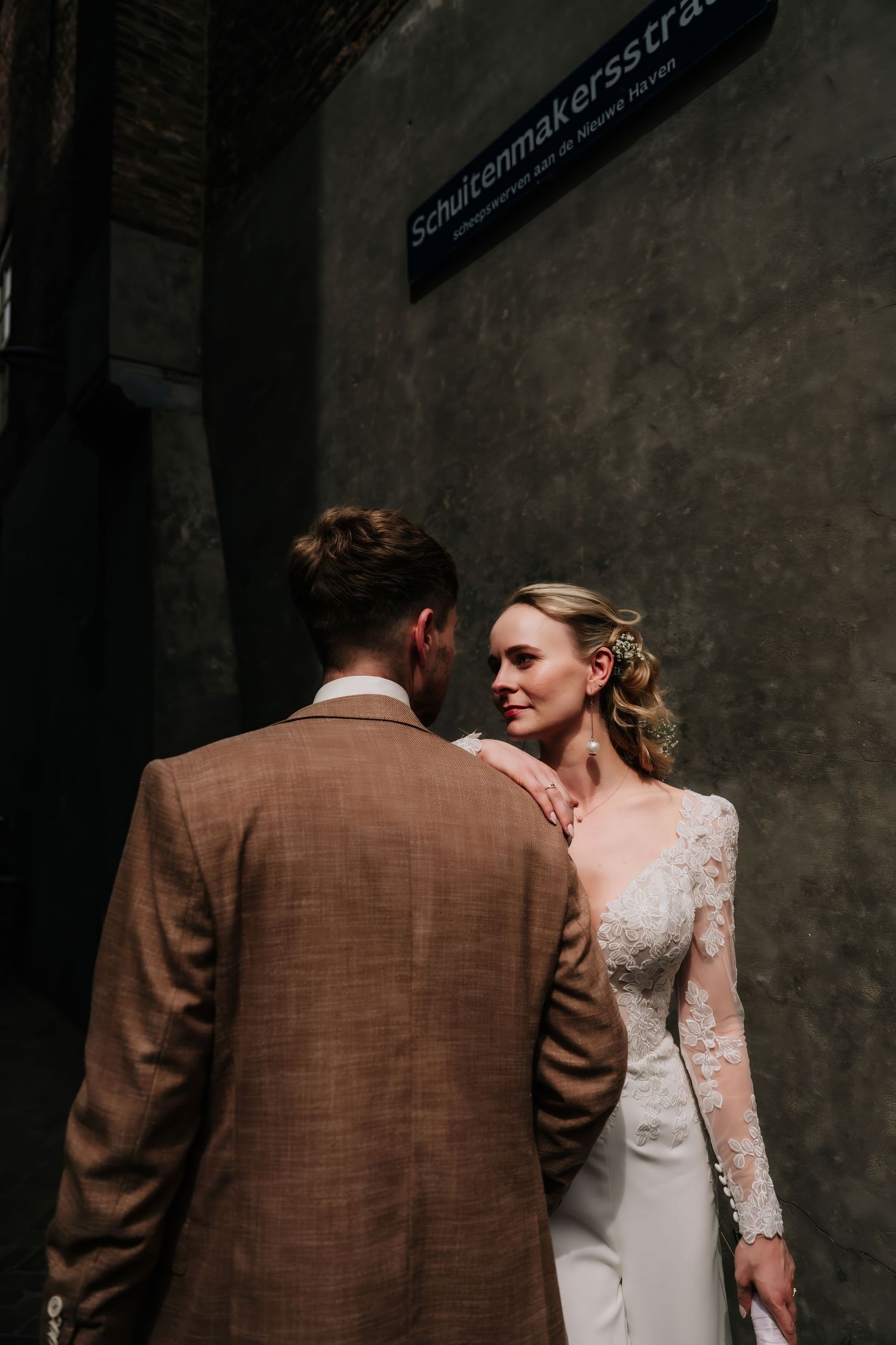 Bride in lace gown and groom in tan suit share an intimate moment on Schultenmakersstrae street.