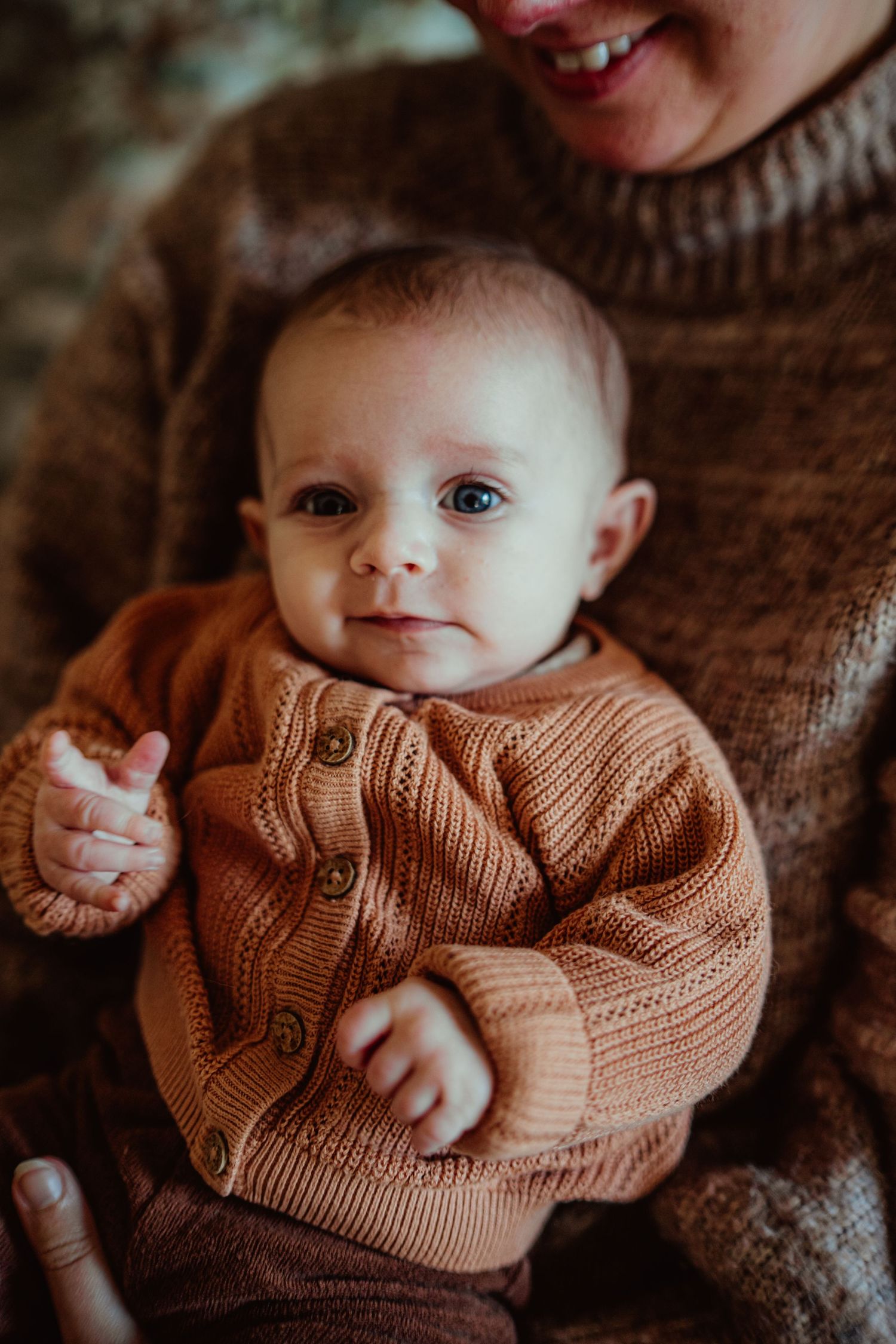 Baby in peach knit cardigan looking directly at camera with bright eyes.
