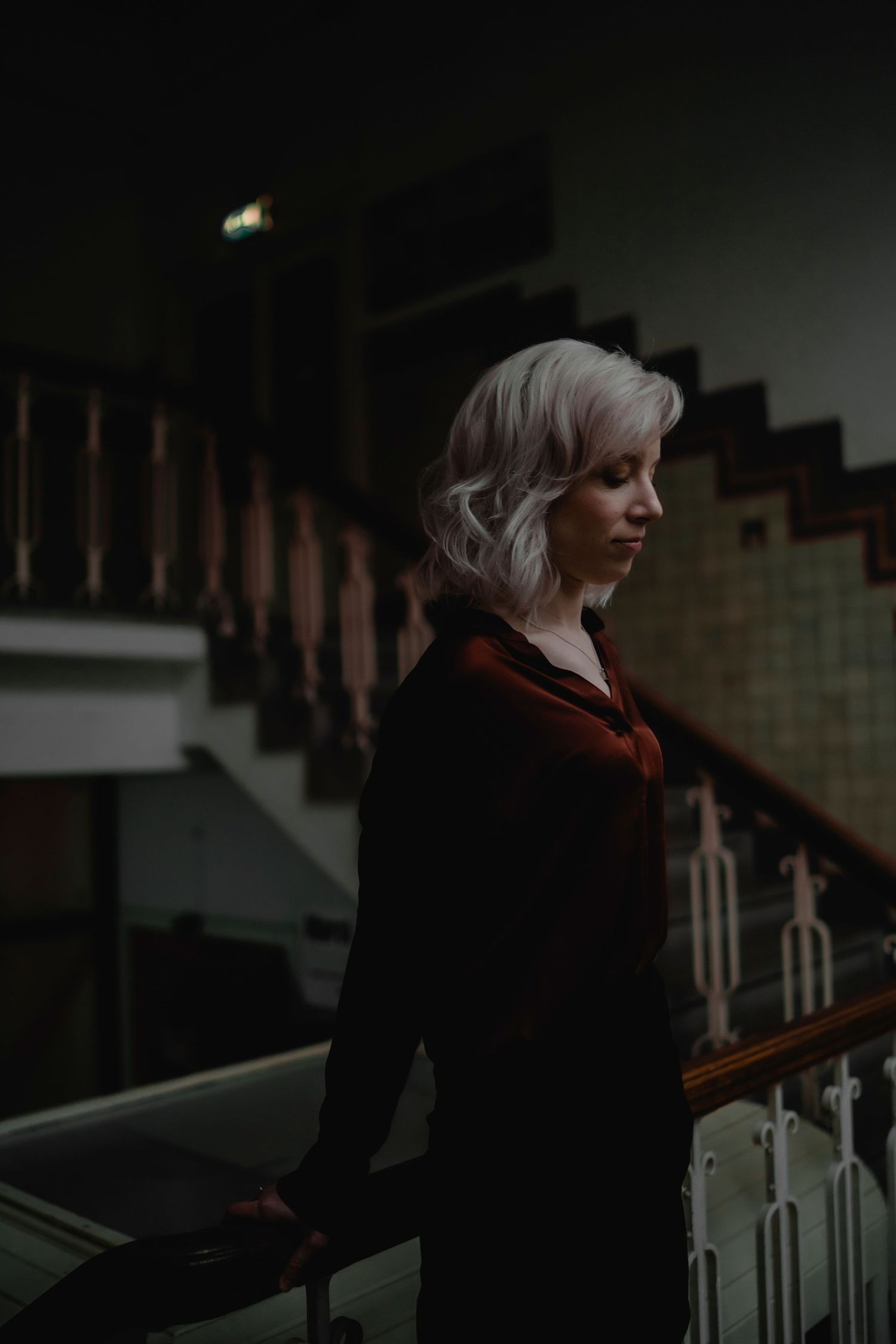 A person in dark clothing sits on white stairs in a dimly lit interior space.