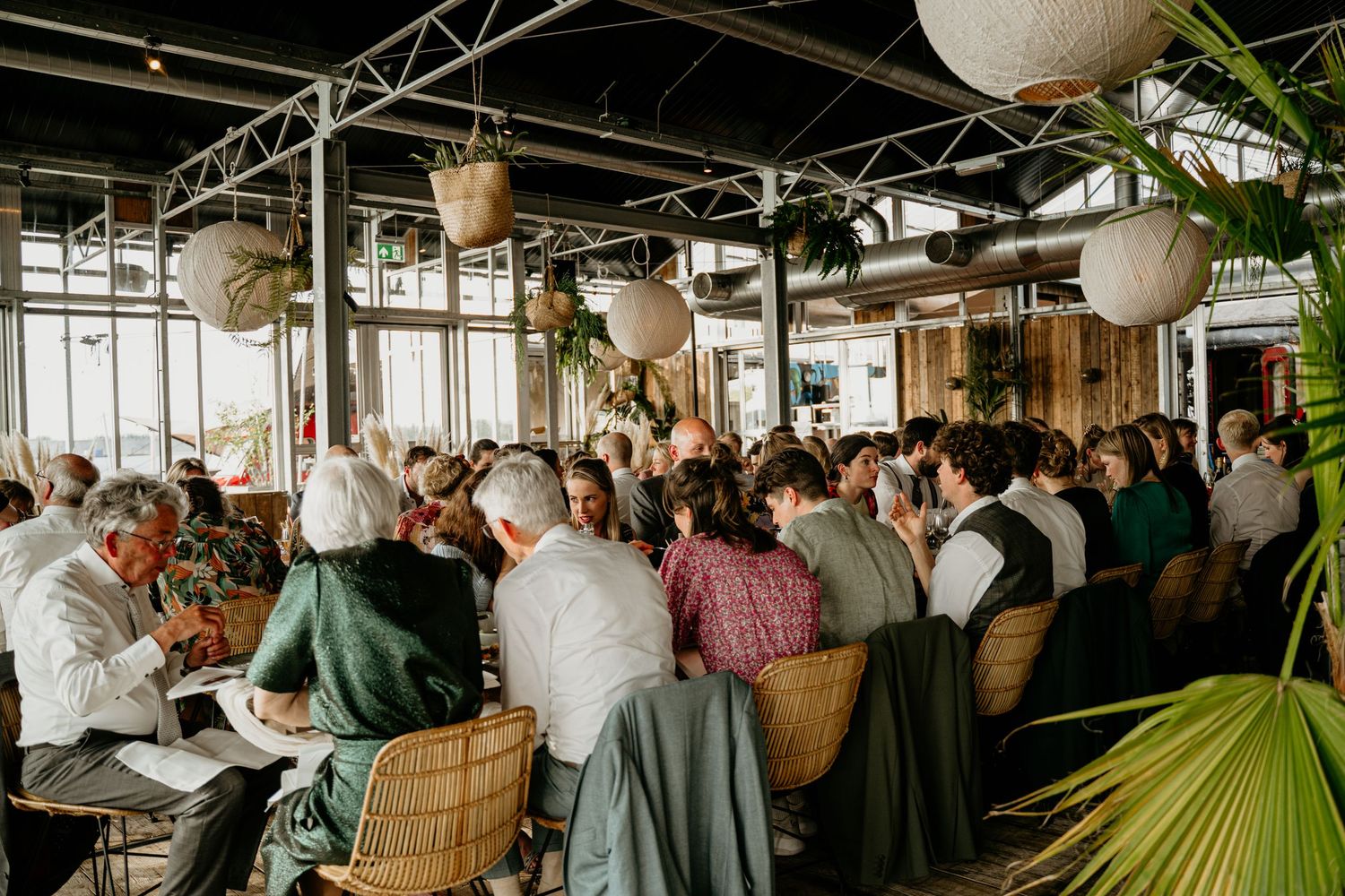 Wedding reception venue with paper lanterns and guests mingling under industrial ceiling.